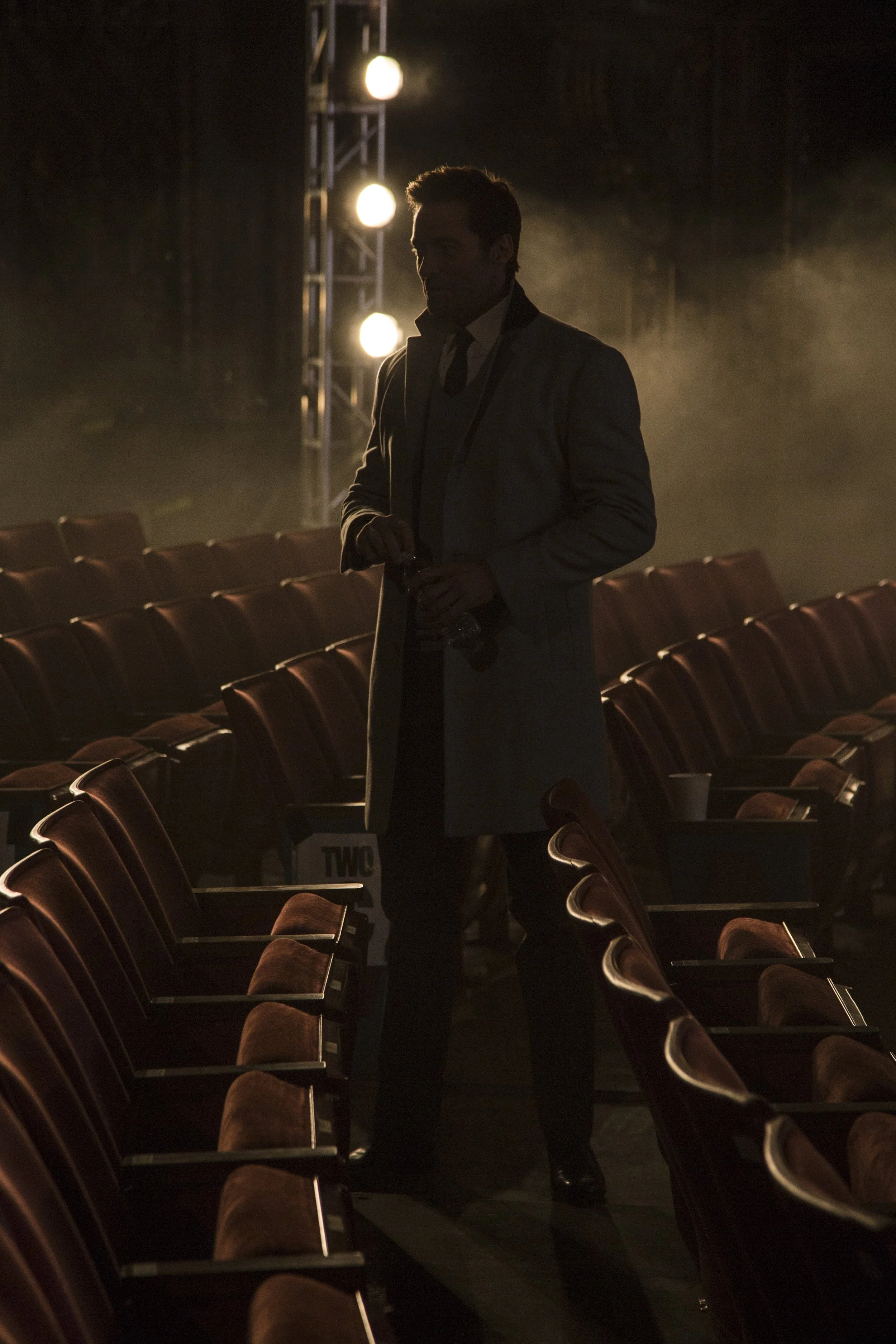 Une silhouette d'homme dans une salle de théâtre ou de cinéma vide, éclairée par des lumières derrière lui.
