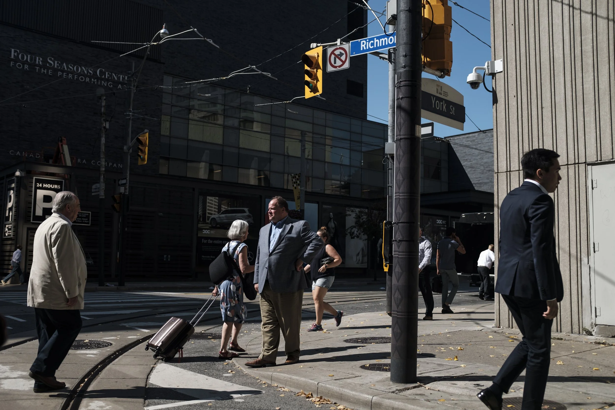 Scène de rue urbaine avec plusieurs passants, échangeurs et panneaux de signalisation, notamment 'Richmond' et 'York St', sous un ciel clair.