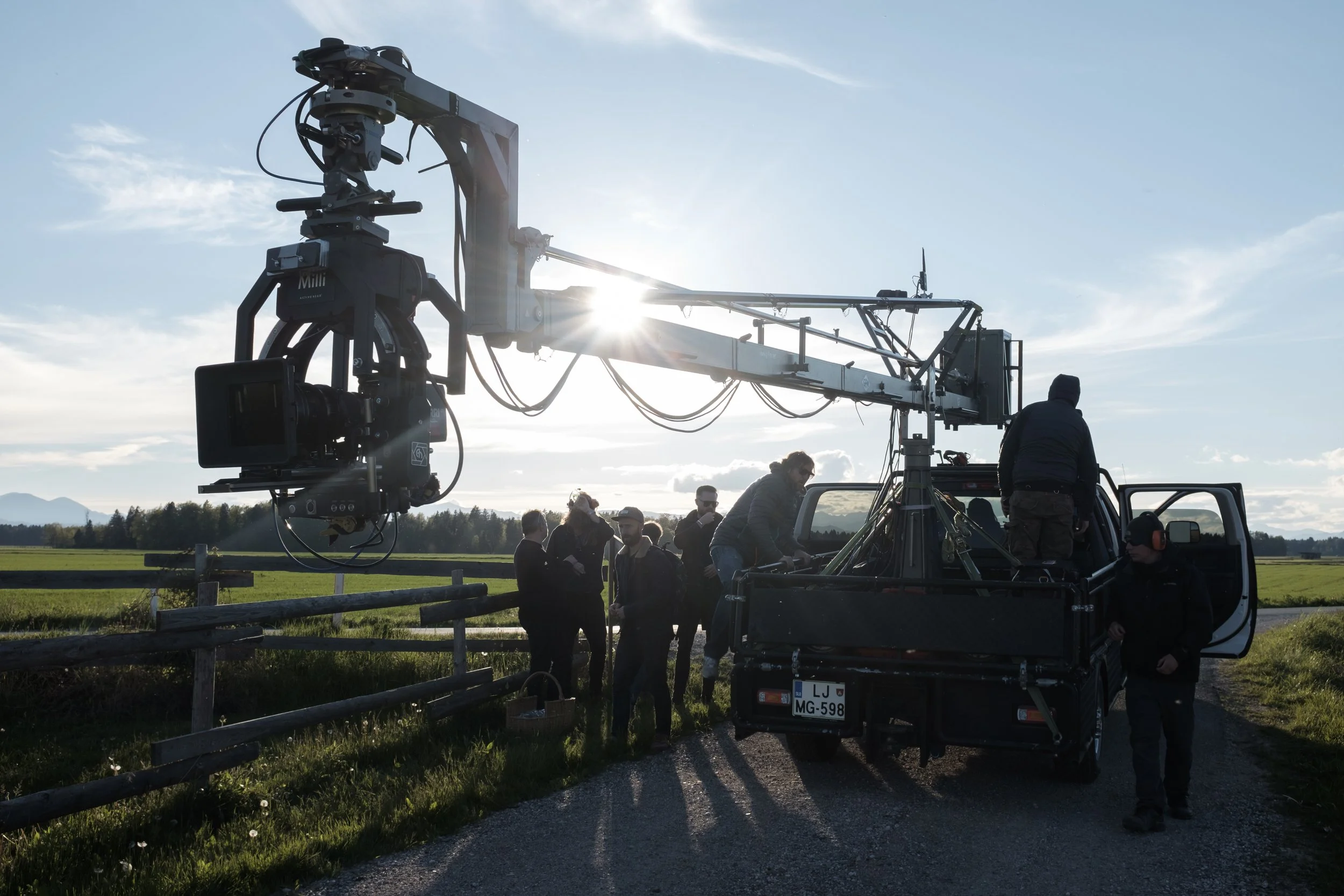 Une équipe de tournage avec une caméra de cinéma montée sur un camion dans un champ, sous un ciel ensoleillé.
