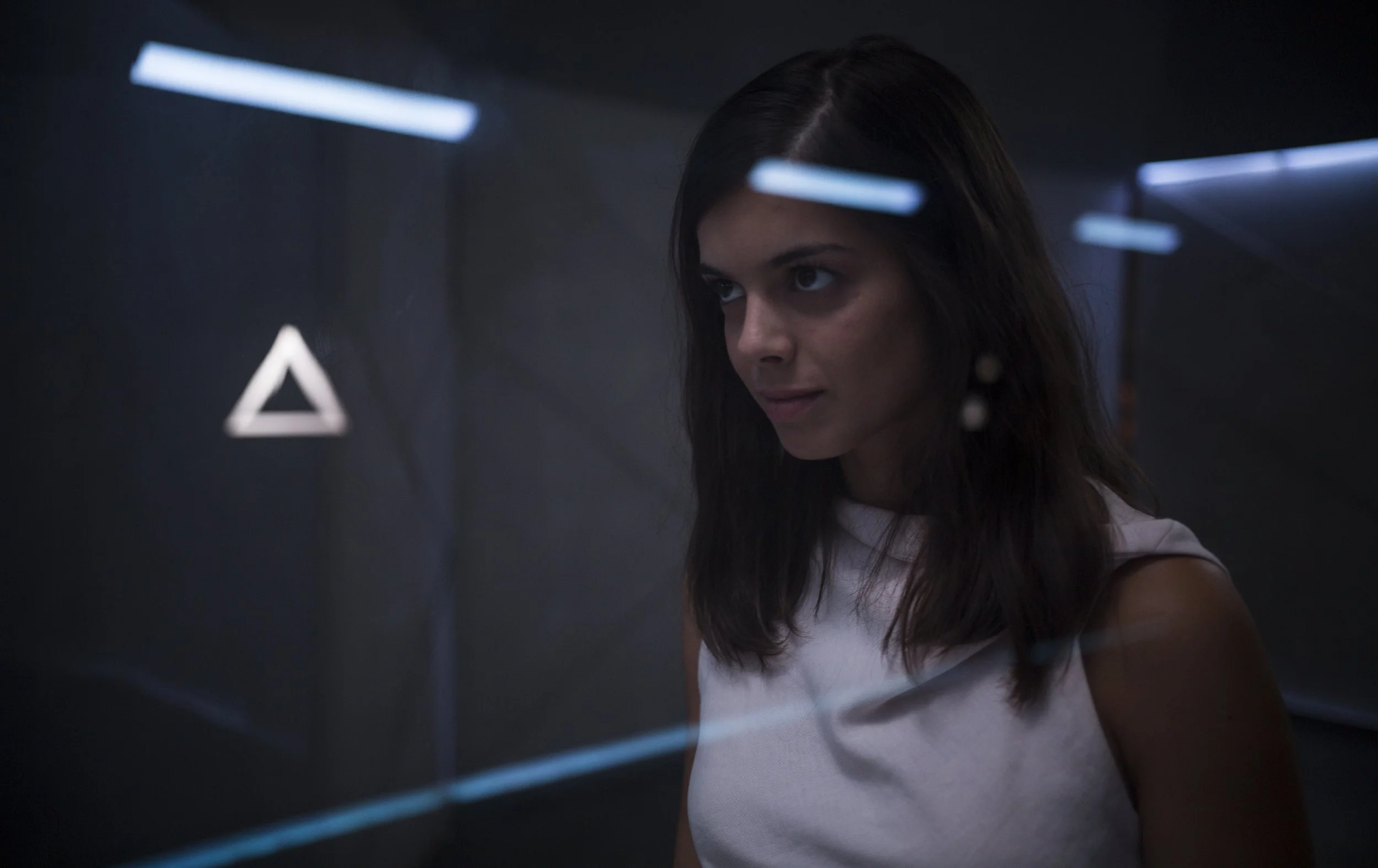 Une femme regarde une interface holographique avec des formes géométriques bleues et blanches dans un environnement sombre.