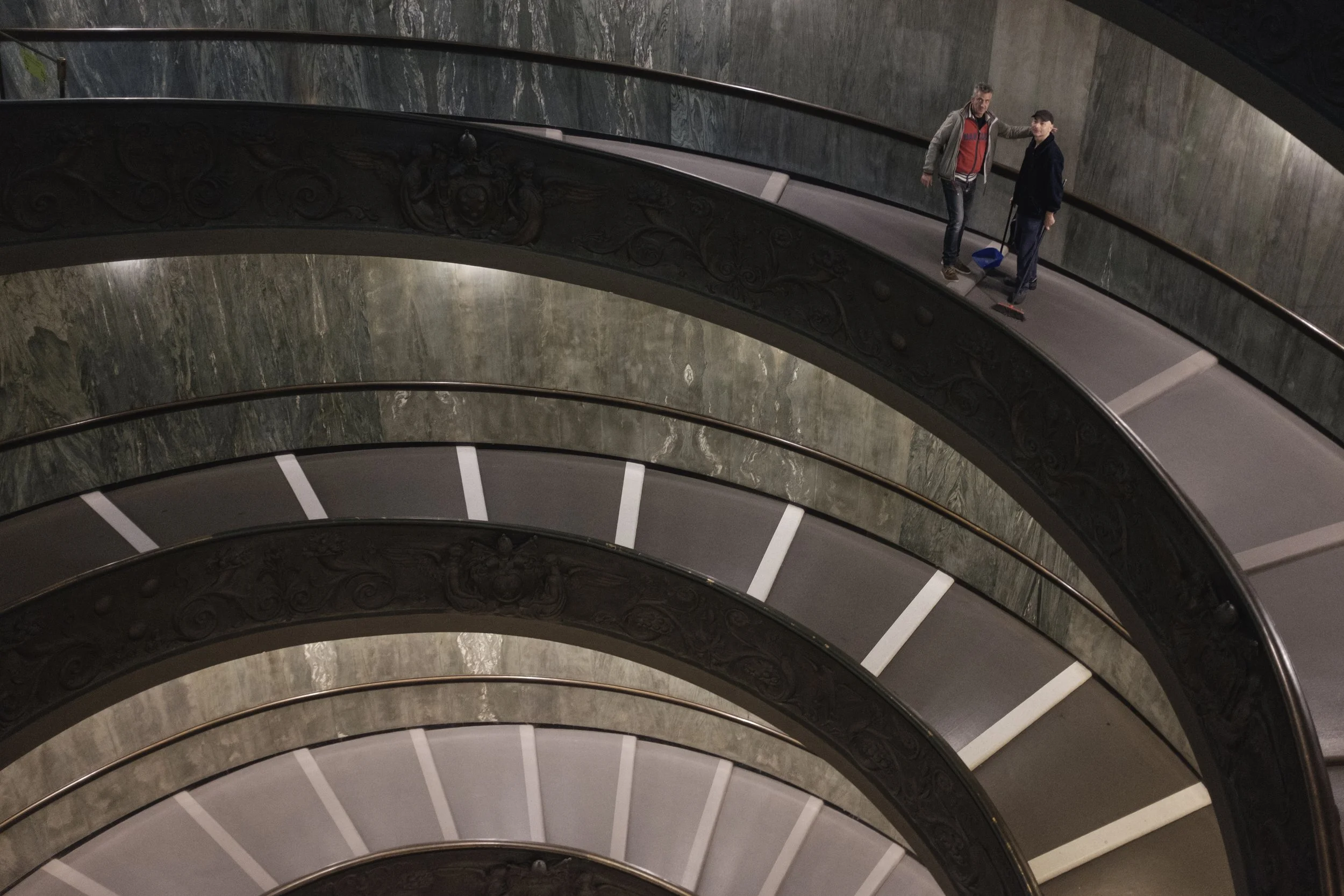 Deux personnes se tenant sur une rampe d'escalier en spirale à l'intérieur d'un bâtiment. 