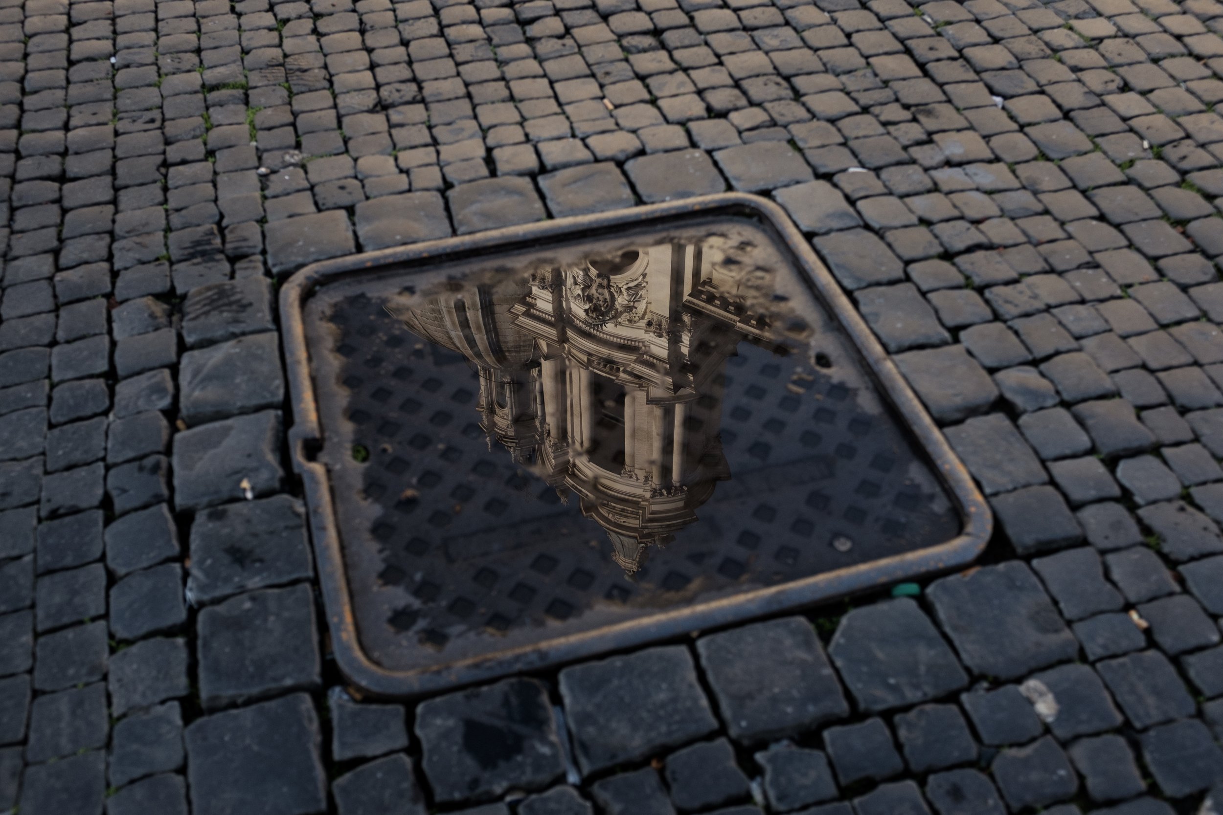 Reflet d'une architecture classique dans une regard de rue sur un sol pavé.