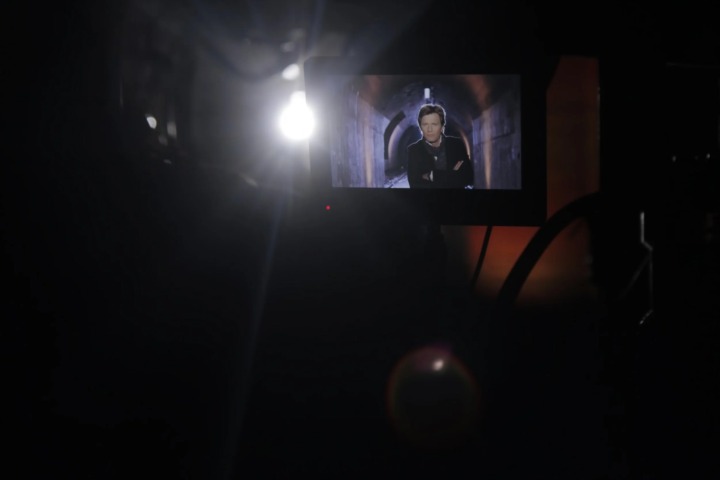 Un écran d'ordinateur dans une pièce sombre affichant une personne dans un tunnel, éclairée par une lumière brillante derrière.