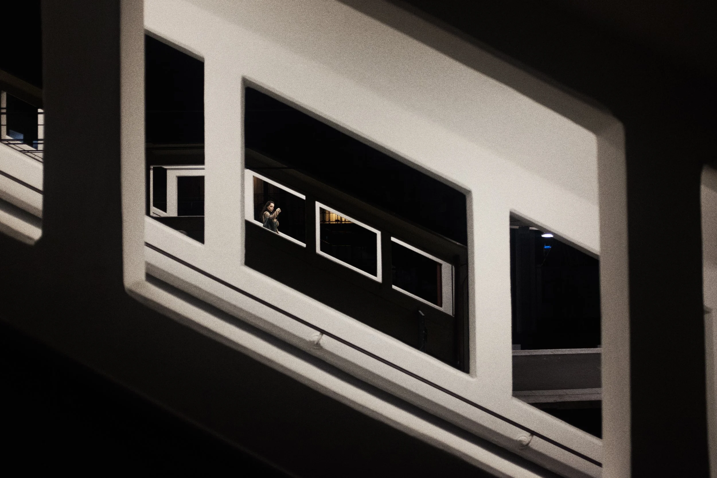 Une femme marchant dans un bâtiment moderne avec des formes géométriques, vue à travers une structure carrée