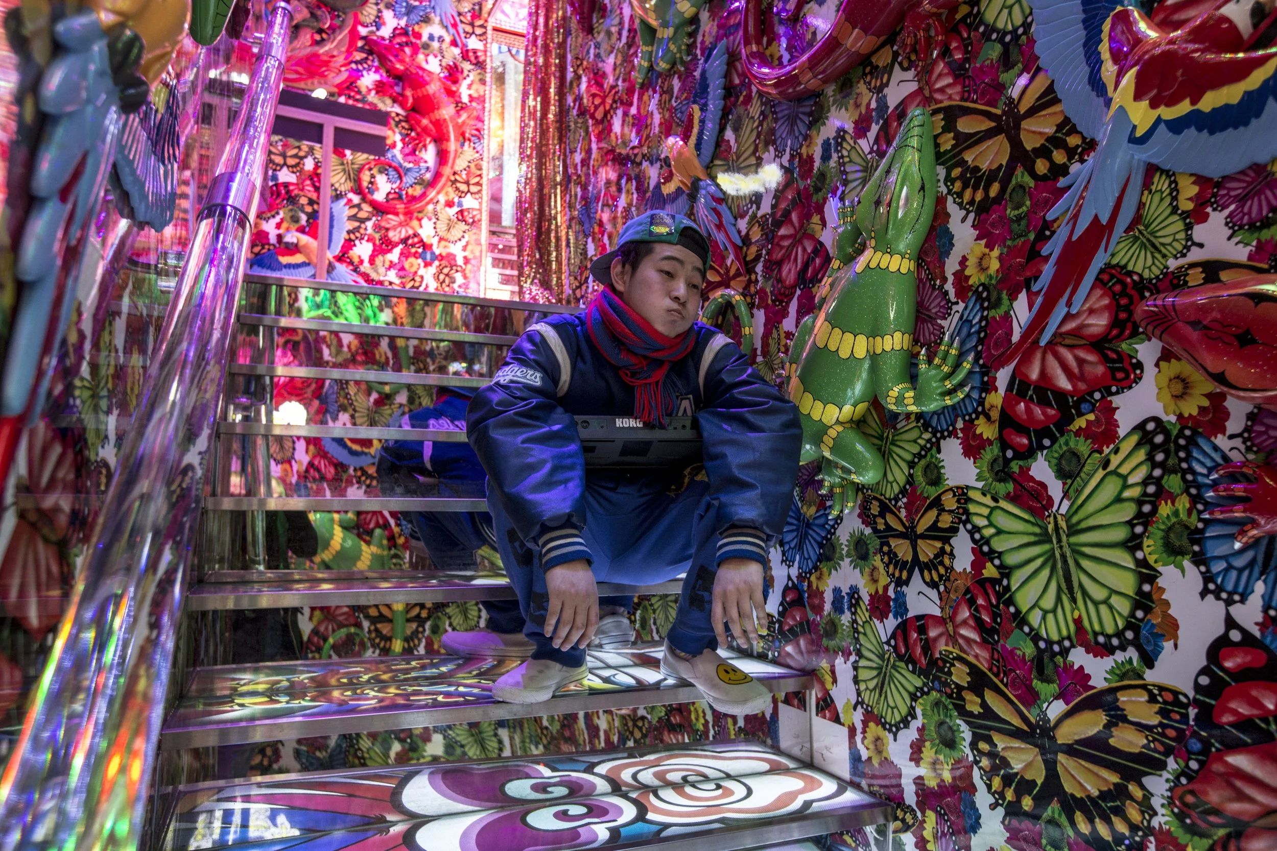 Une personne assise sur un escalier décoré avec des motifs de papillons colorés, dans une pièce également ornée de papillons en relief et de couleurs vives.