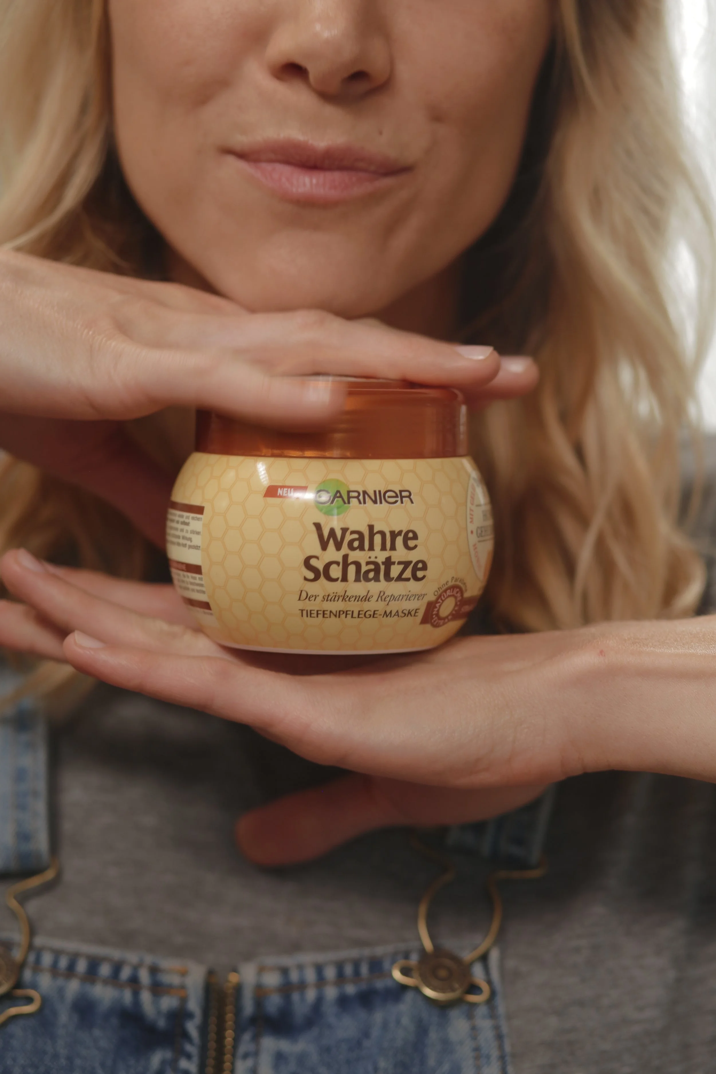 Une femme tient un pot de masque de soin pour les yeux Garnier Wahre Schätze, en souriant.