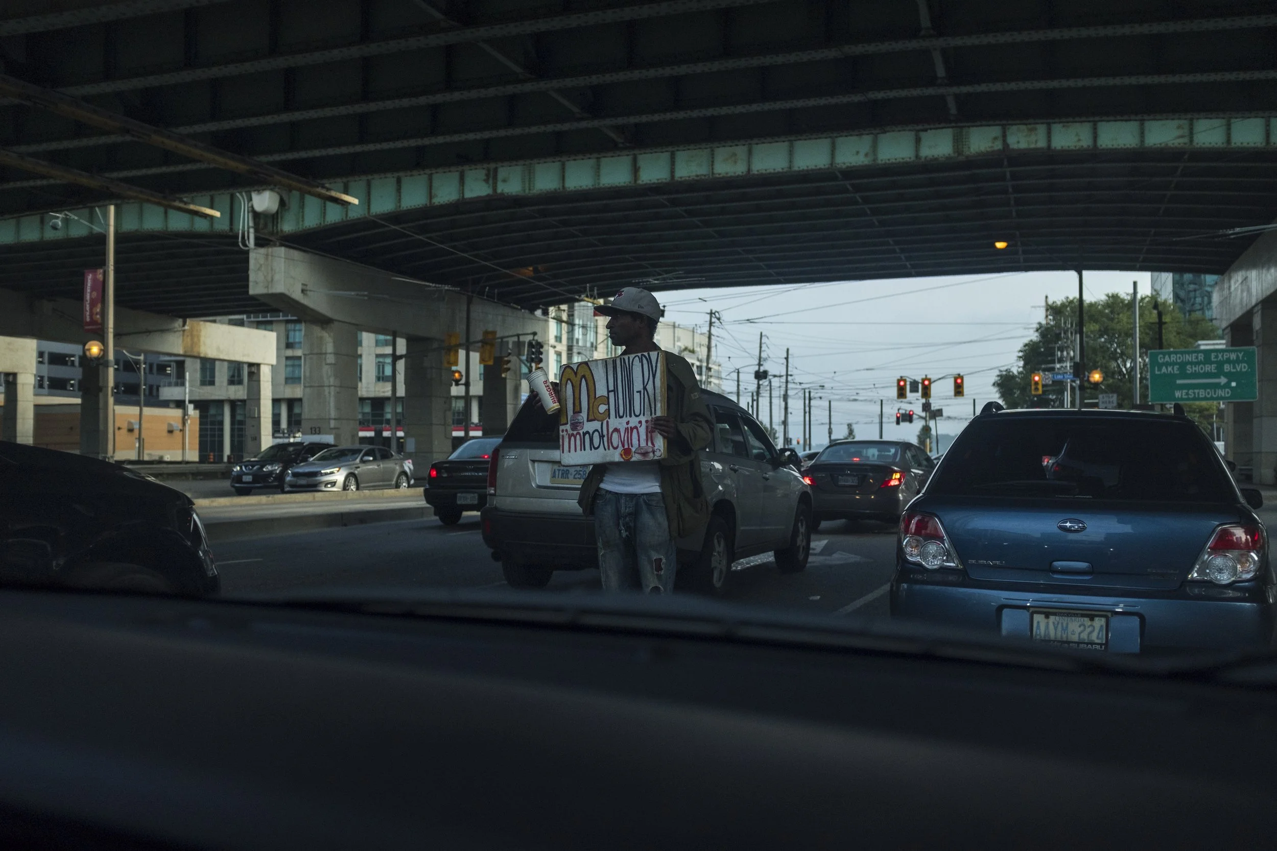 Personne faisant du slogan pour McDonald's tout en tenant une bouteille d'eau, dans une rue urbaine sous un pont, le soir.