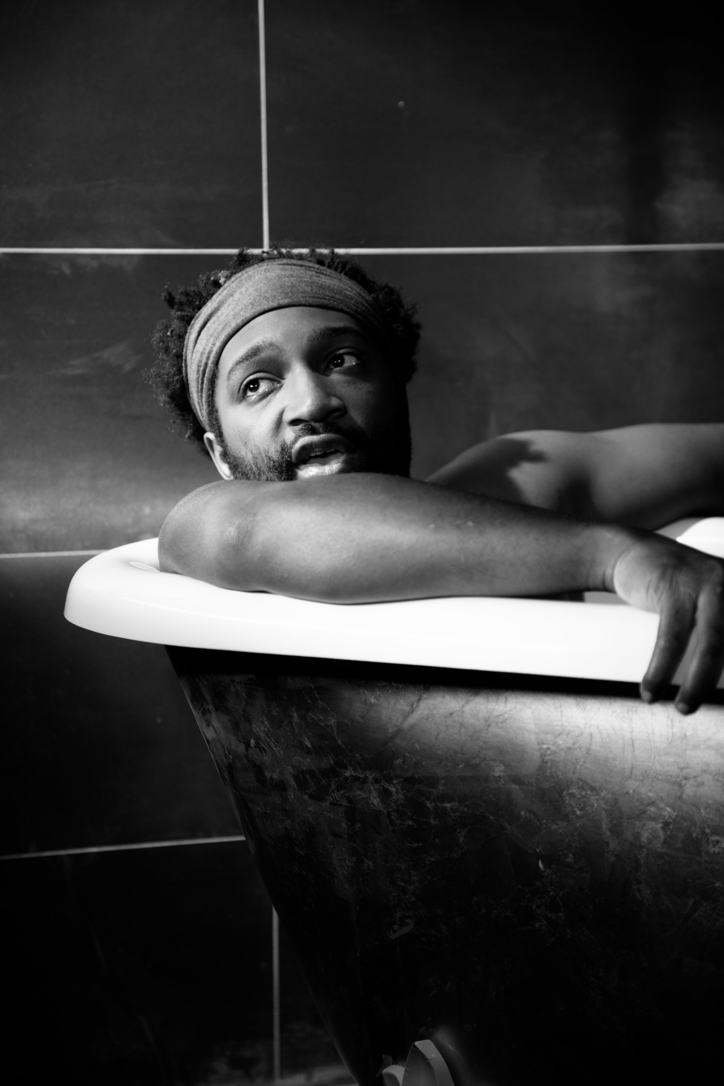 Homme noir dans une baignoire en cuir, appuyé sur le rebord, regardant vers le haut, tête coiffée d'un bandeau