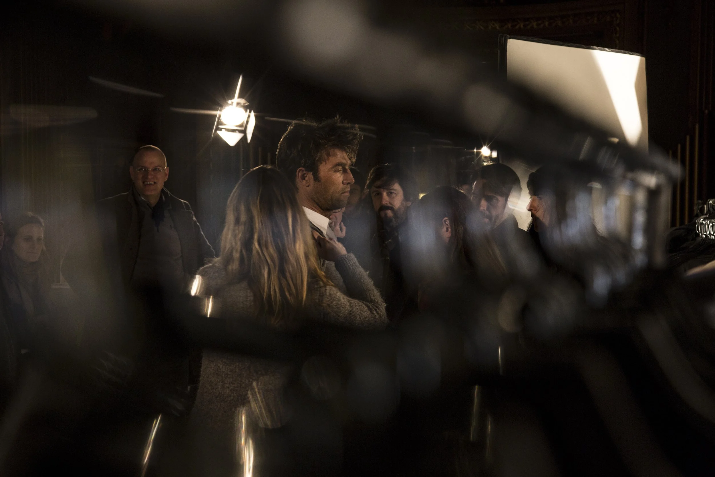 Une scène de tournage ou de production cinématographique avec plusieurs acteurs ou membres de l'équipe, vue à travers un objectif ou un filtre, avec des lumières fortes en arrière-plan.