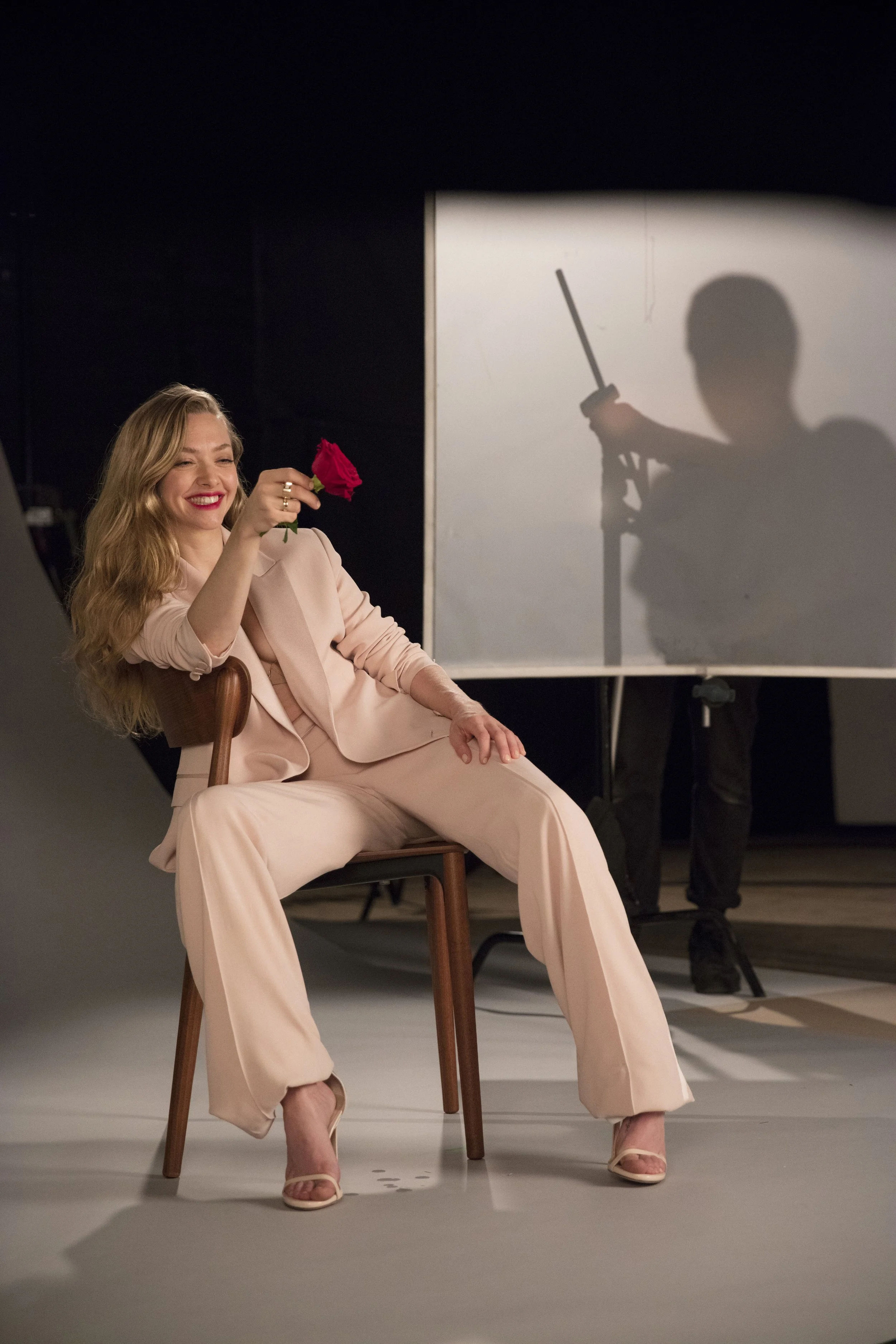 Une femme souriante assise sur une chaise, tenant une rose rouge, dans un studio de photographie.