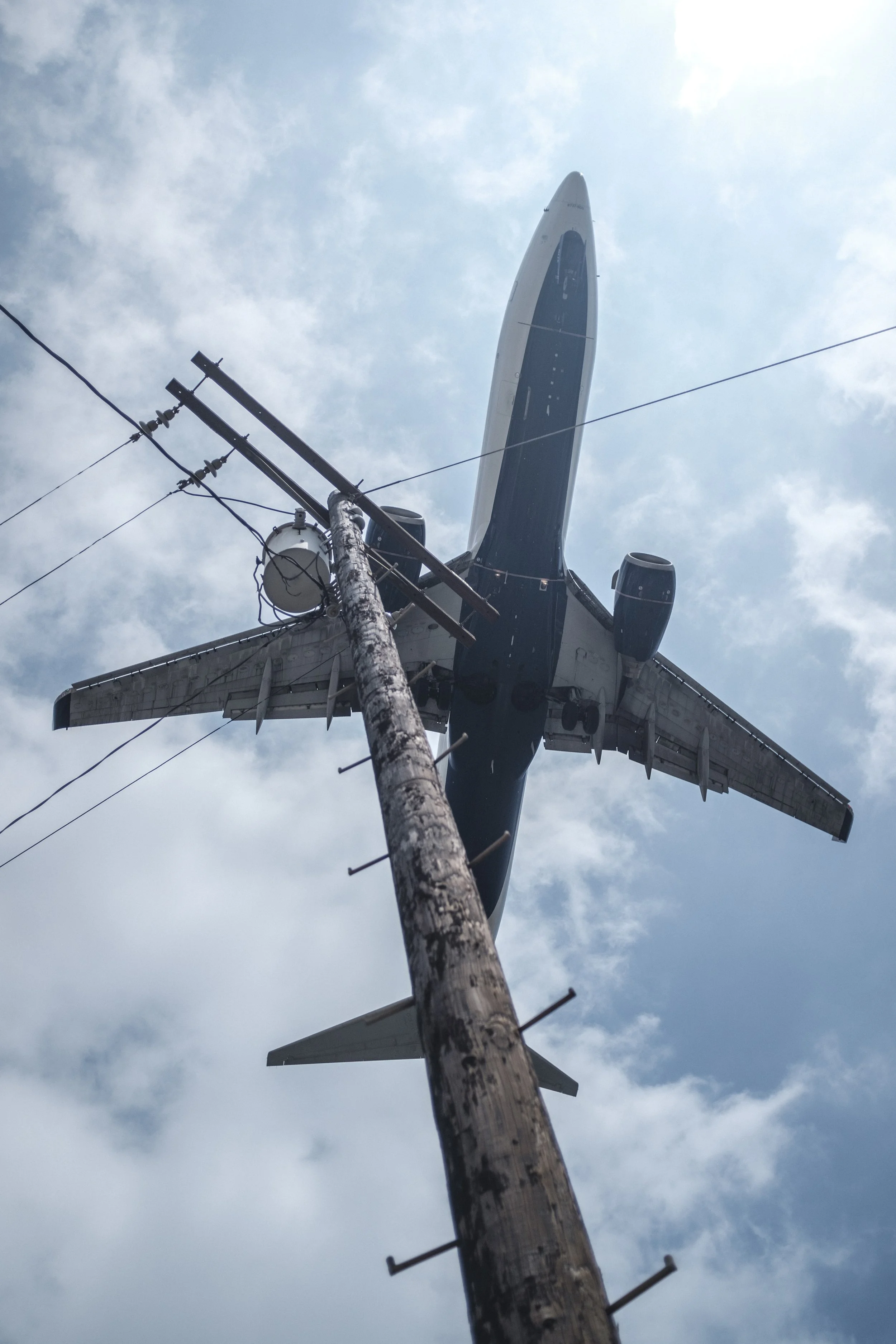 Un avion de ligne vole dans le ciel bleu par-dessus un poteau électrique en bois.