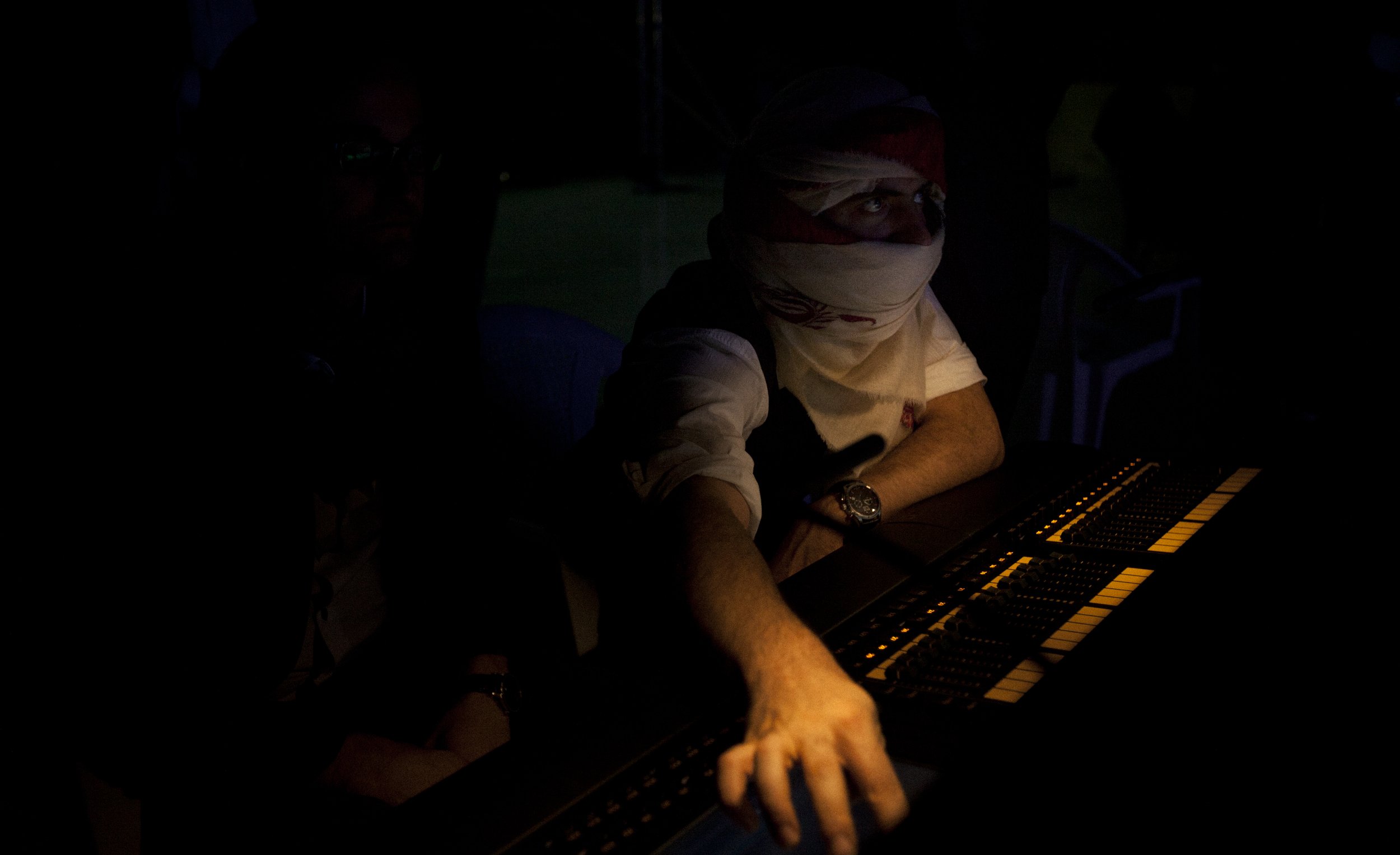 Personne utilisant un contrôleur de musique dans une pièce sombre, portant un bandeau sur la tête et un bracelet, avec un éclairage minimal sur le clavier.