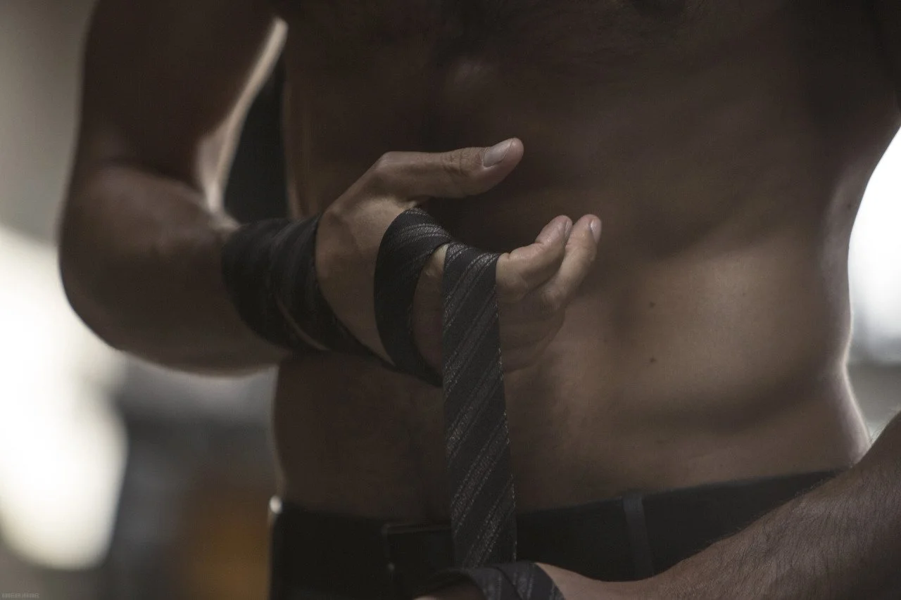 Un homme avec un torse musclé qui porte une cravate noire enroulée autour du poignet