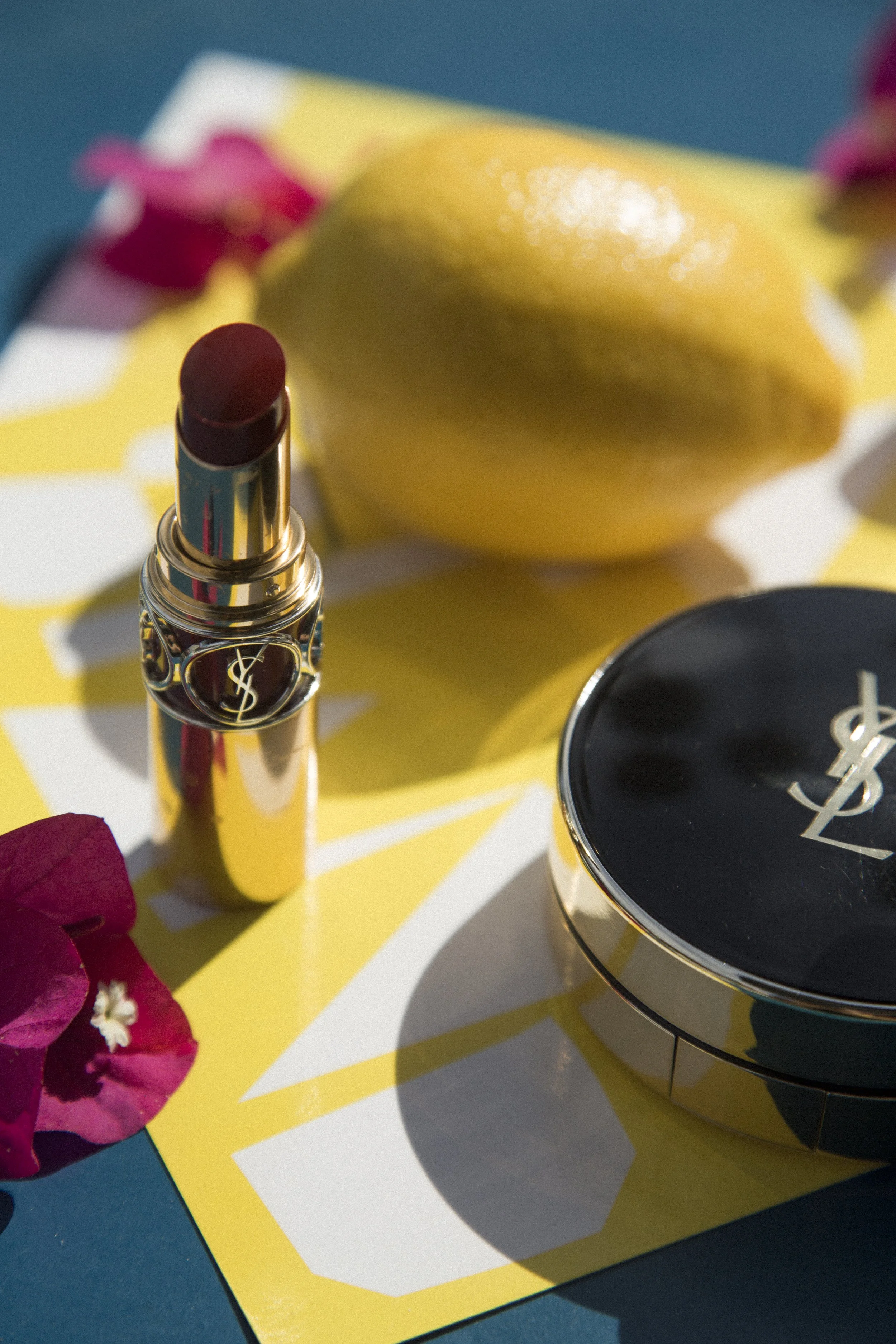 Rouge à lèvres Yves Saint Laurent, boîte de maquillage YSL, citron jaune, fleurs roses sur un fond coloré.