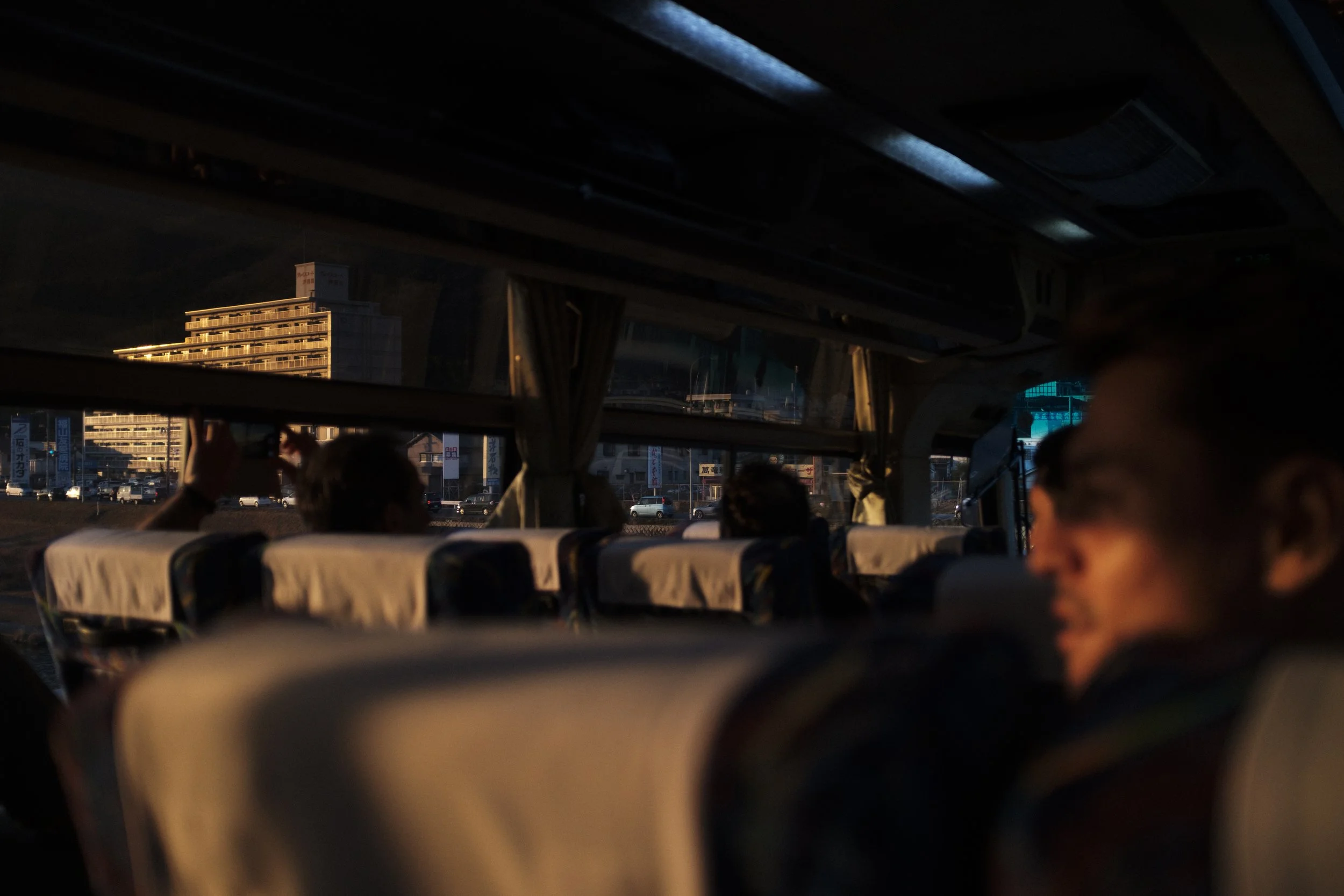 À l'intérieur d'un bus de nuit avec des passagers, vue à travers la fenêtre avec des bâtiments illuminated au coucher du soleil.