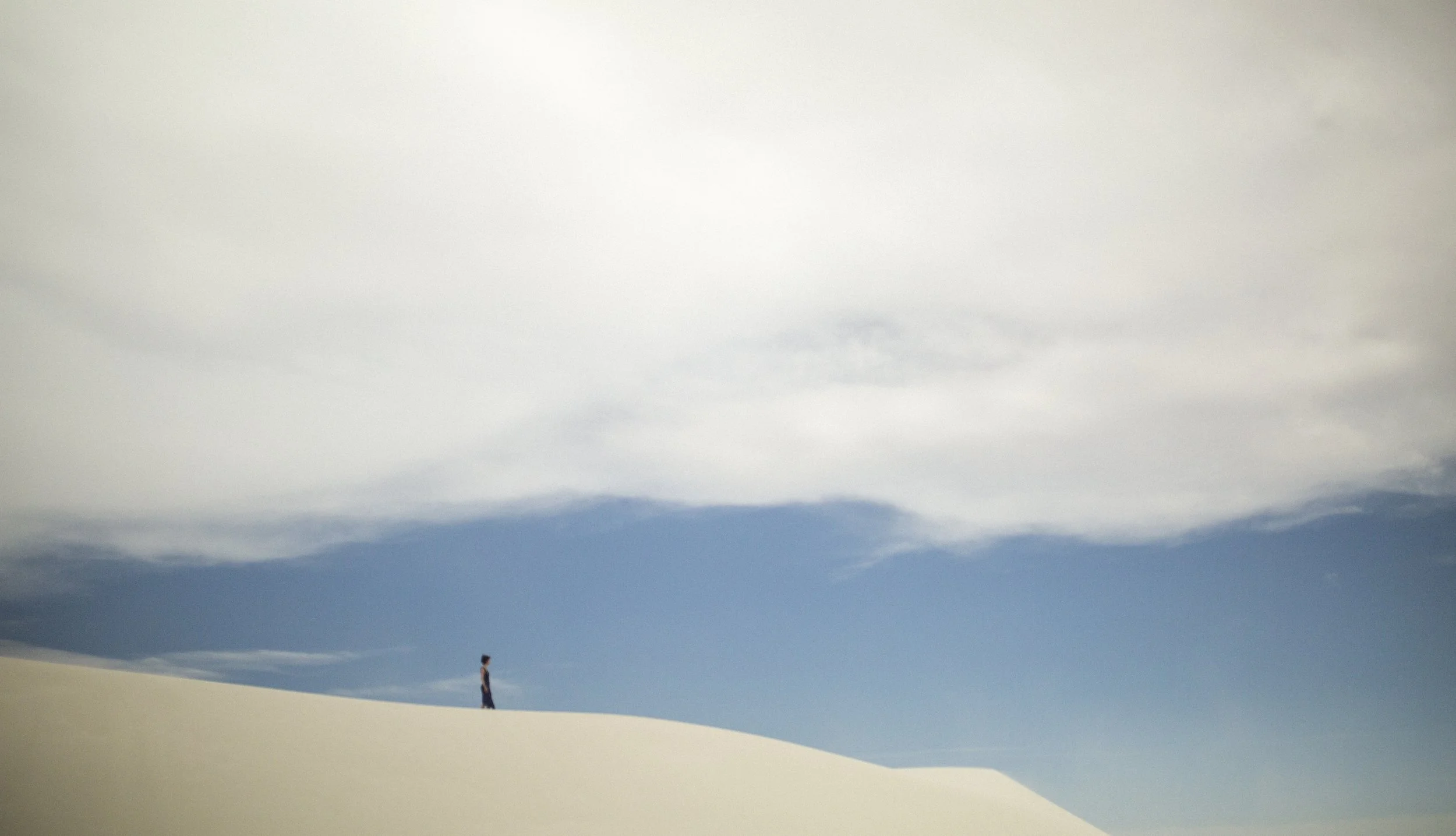 Une personne se tient seule sur une dune de sable sous un ciel partiellement nuageux.