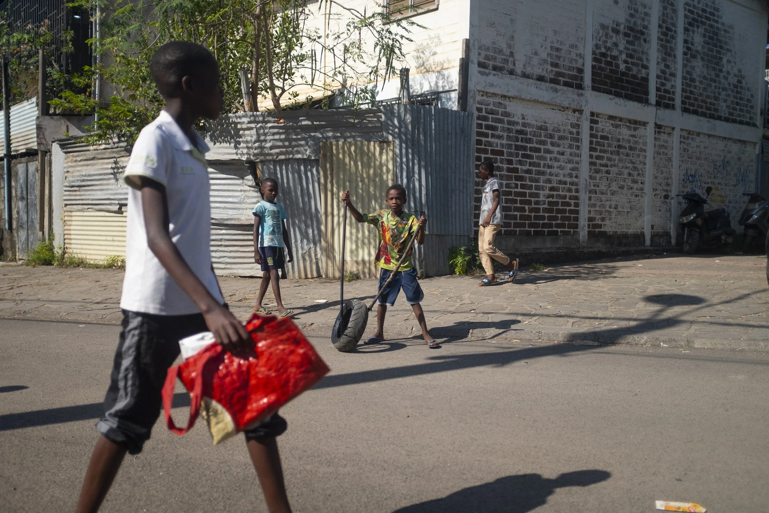Enfants jouant dans une rue urbaine, avec certains utilisant des pneus comme jouets et d'autres marchant ou observant, dans un environnement résidentiel en arrière-plan.