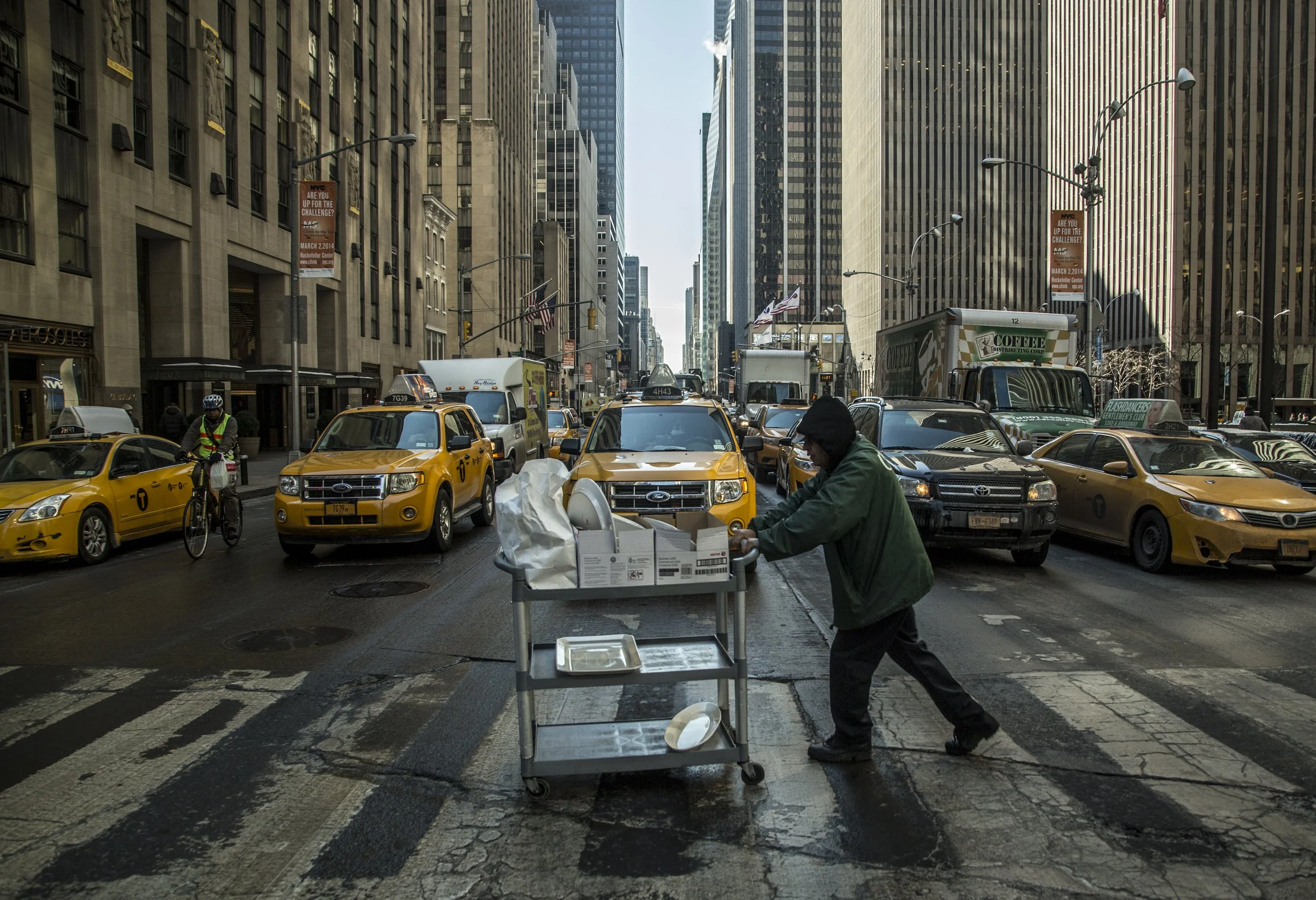 Une rue animée avec des taxis jaunes, des véhicules et des piétons. Un homme pousse un chariot d'alimentation dans la rue, entouré de hauts bâtiments urbains.