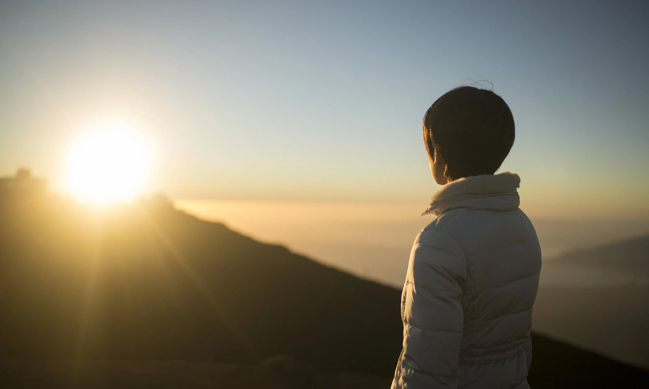 Une personne regardant le coucher du soleil sur un paysage de montagne.