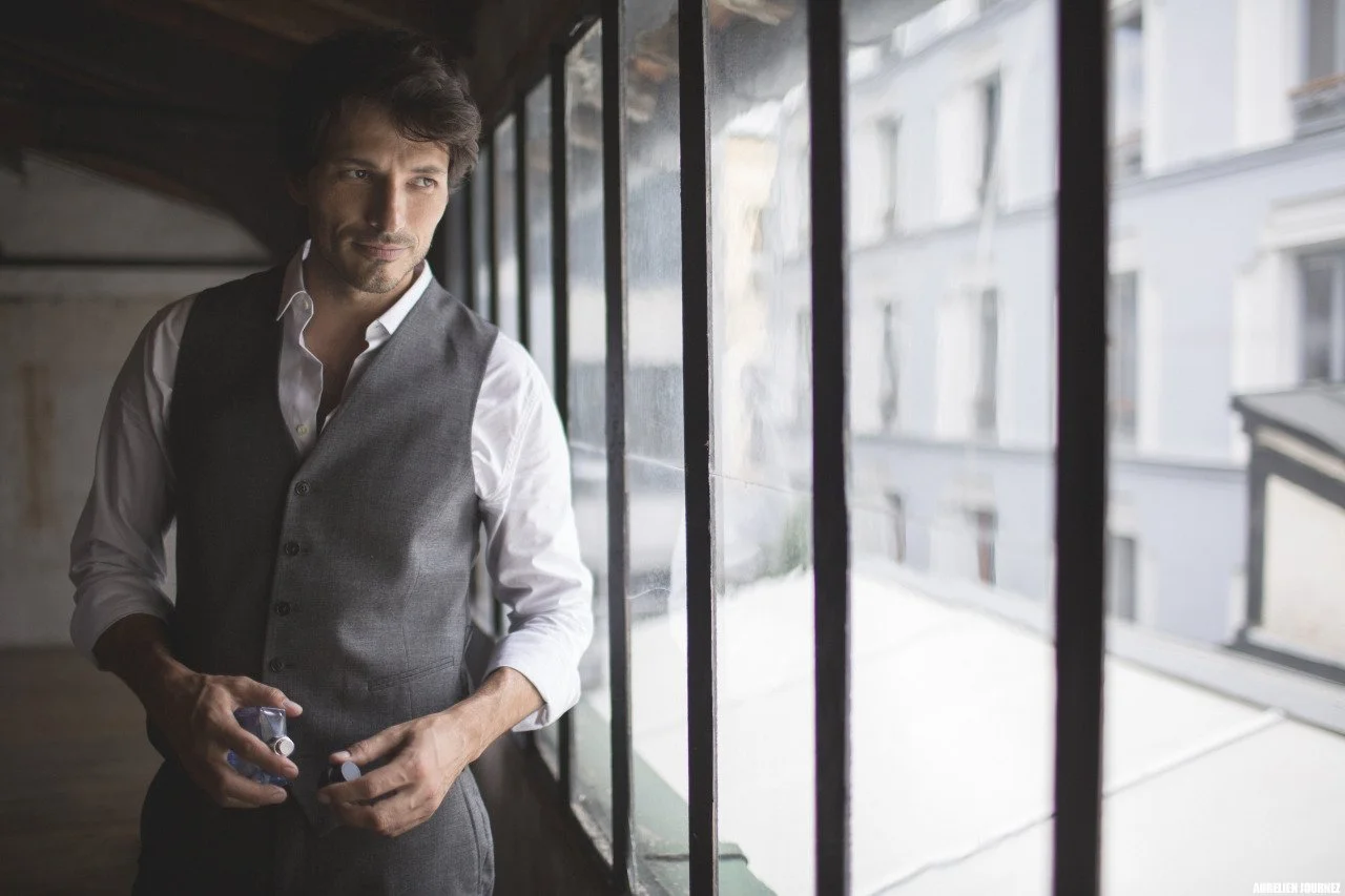 Un homme en tenue professionnelle se tient près d'une grande fenêtre dans un intérieur avec vue sur des bâtiments résidentiels.