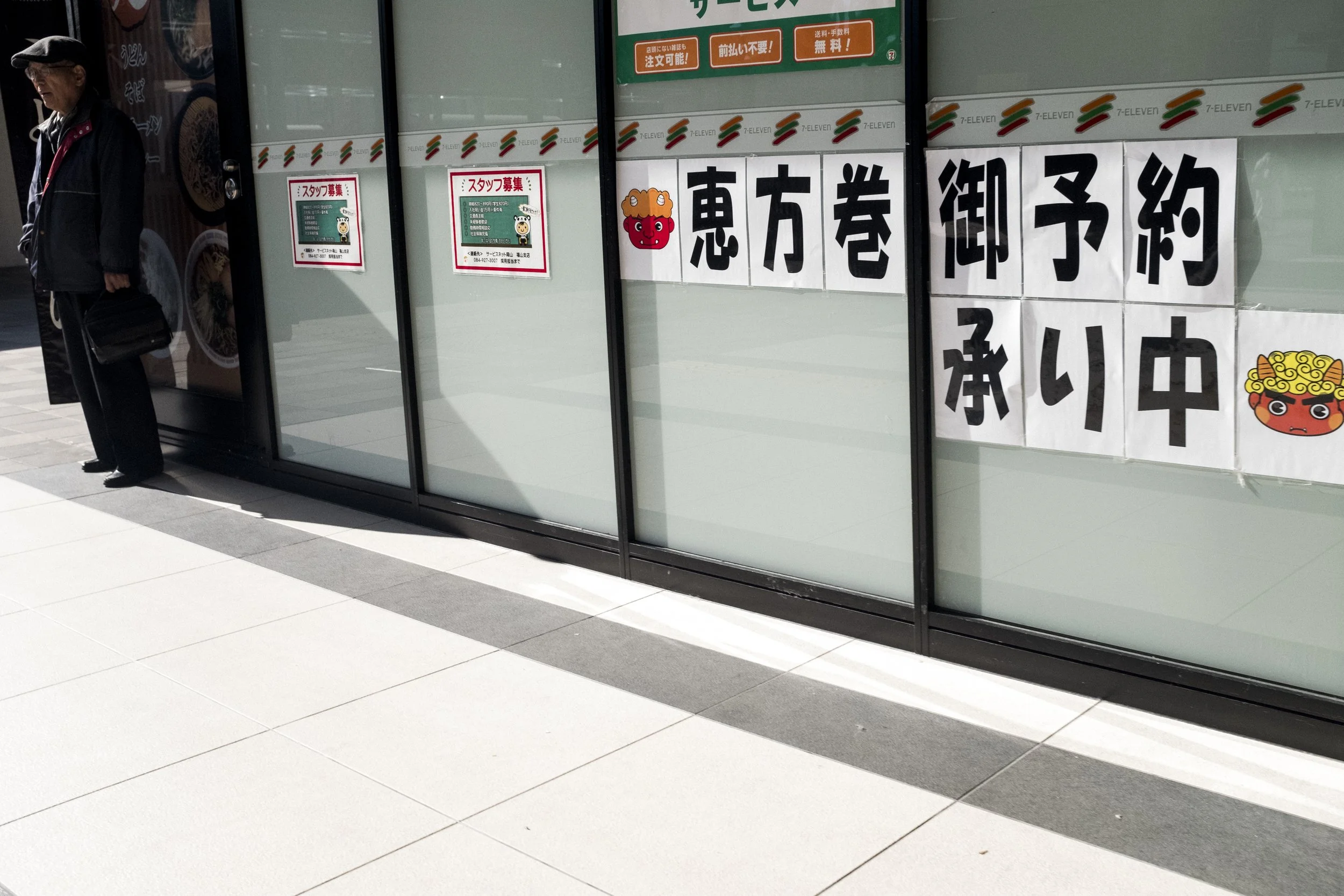 Fenêtre d'une boutique 7-Eleven avec avis en japonais indiquant que la réservation est en cours, décorée avec des illustrations de personnages de style traditionnel japonais.