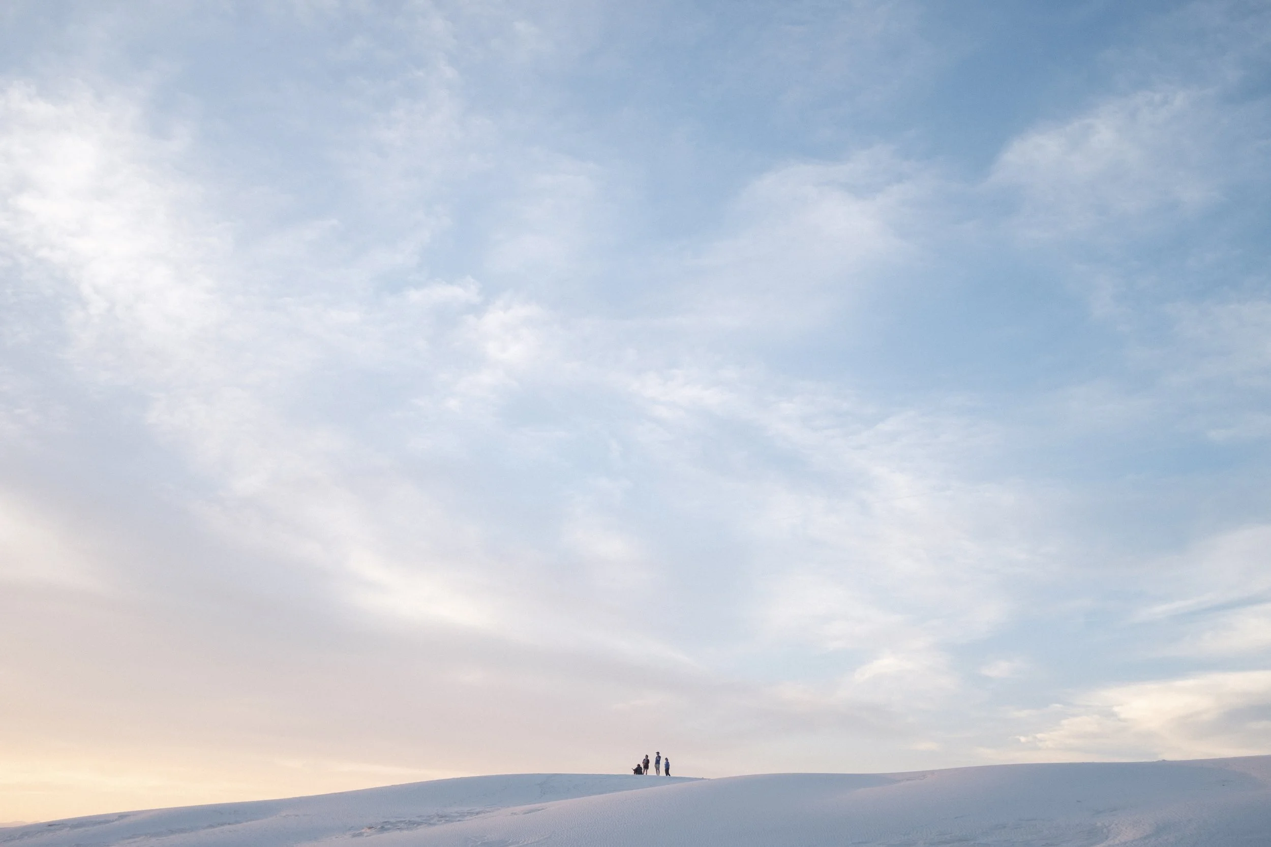 Trois personnes se tiennent sur une colline enneigée sous un ciel partiellement nuageux au coucher du soleil.