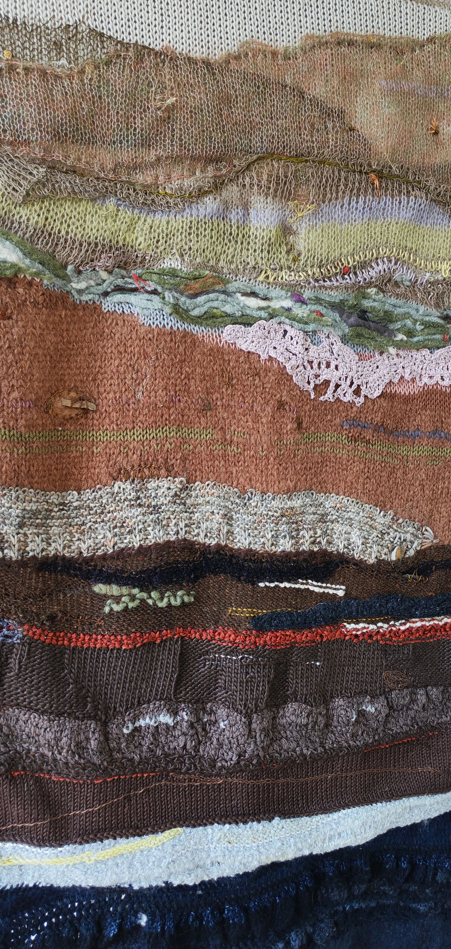 Close-up of a layered textile art wall hanging with various textures and patterns. The photo shows hand and machine knitting, crochet, found objects and stitching as some techiniques used in making it.