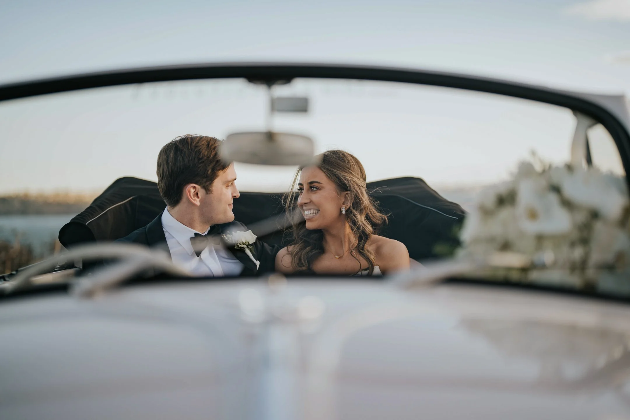 A couple is sitting in a car, smiling at each other, with a scenic view in the background.
