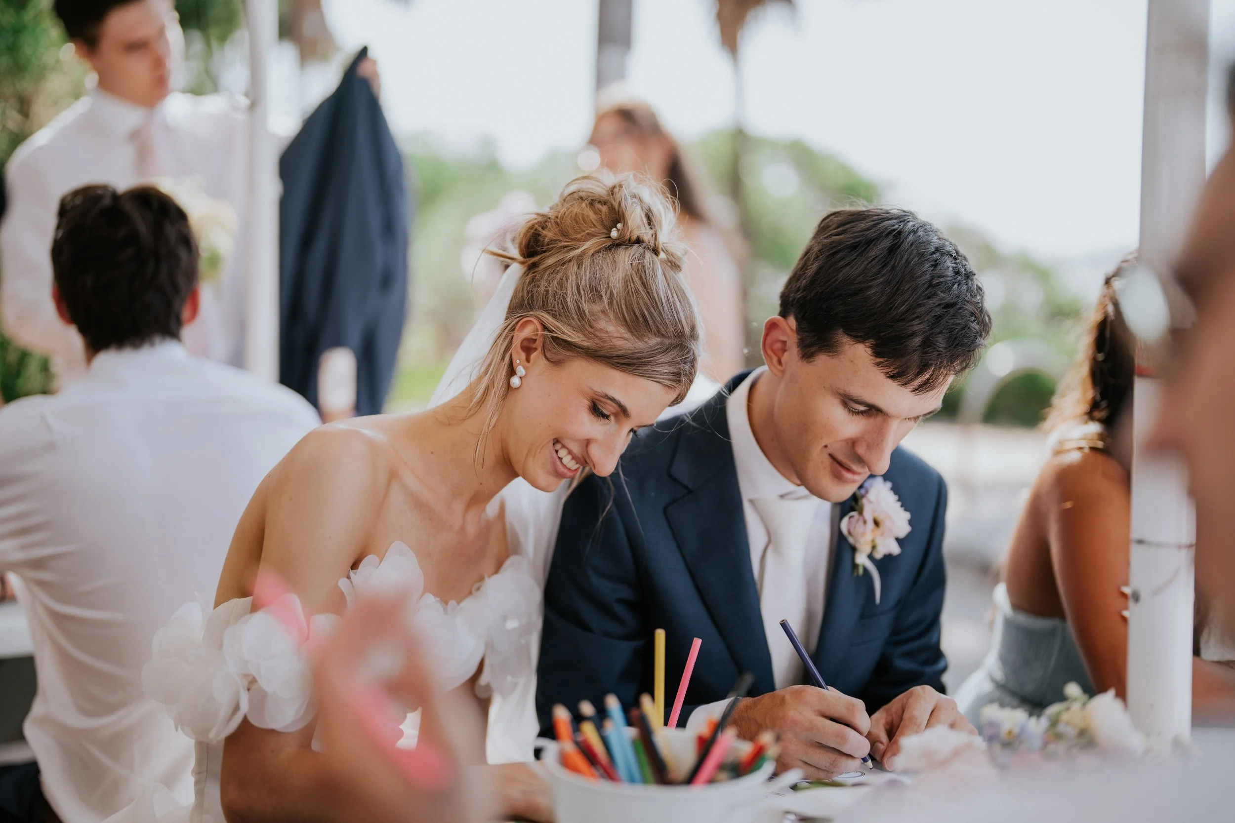 A bride and groom signing documents at a wedding reception with friends and family around, celebrating outdoors.