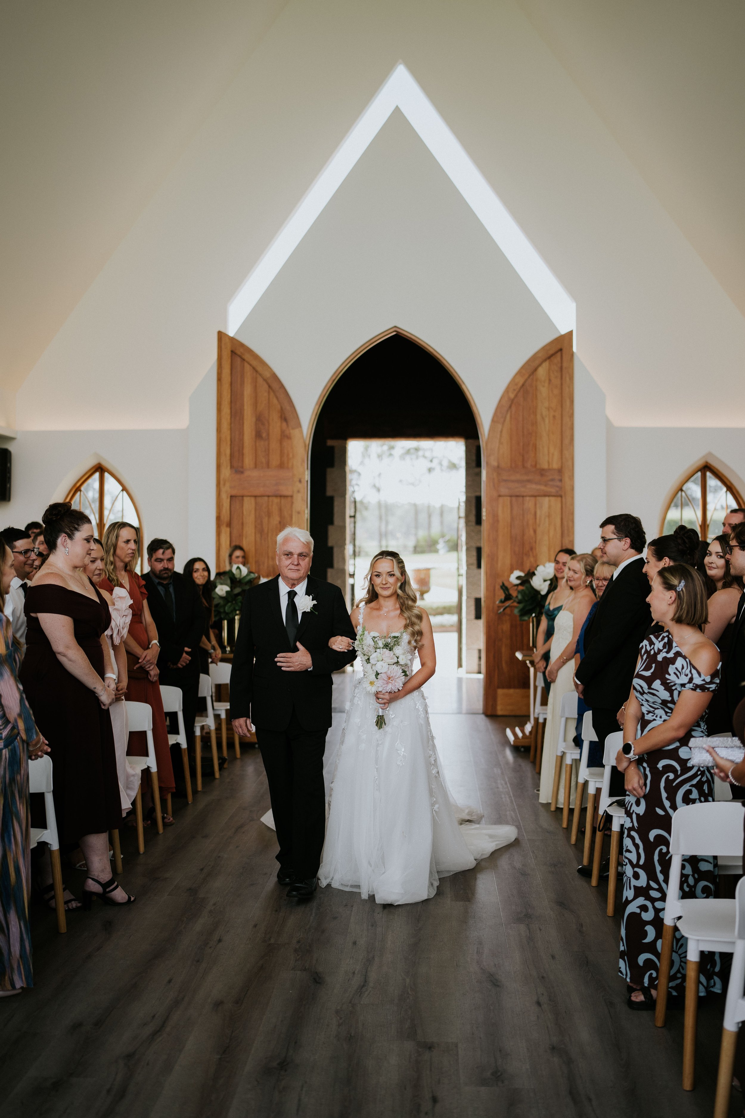 A bride walking down the aisle with her father in a church during her wedding ceremony, surrounded by guests on either side.
