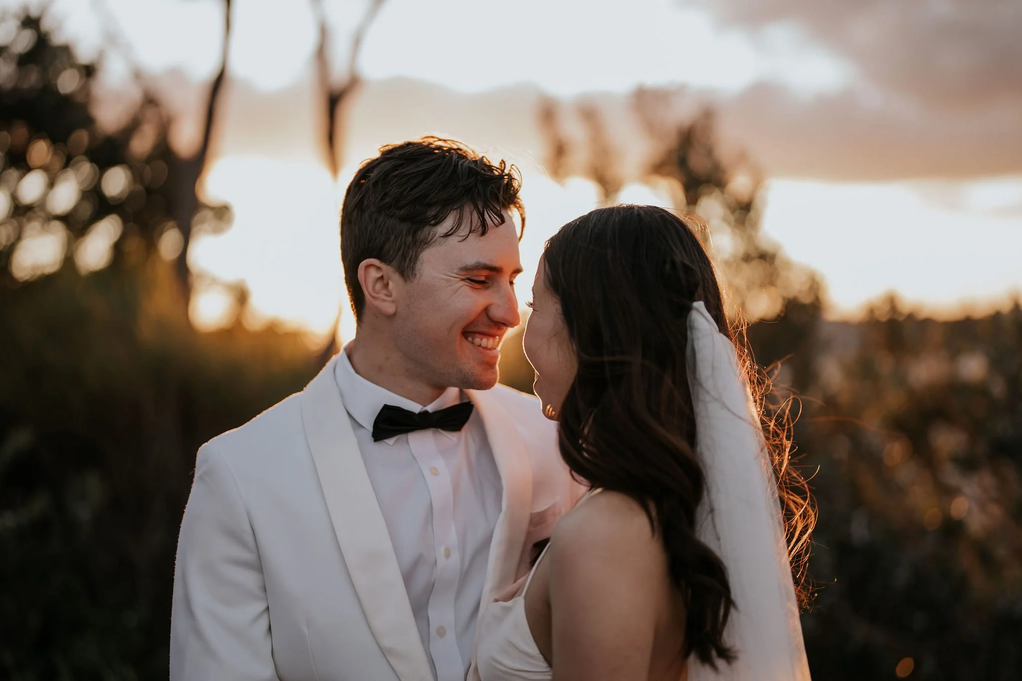A happy couple in wedding attire sharing a close moment outdoors during sunset.