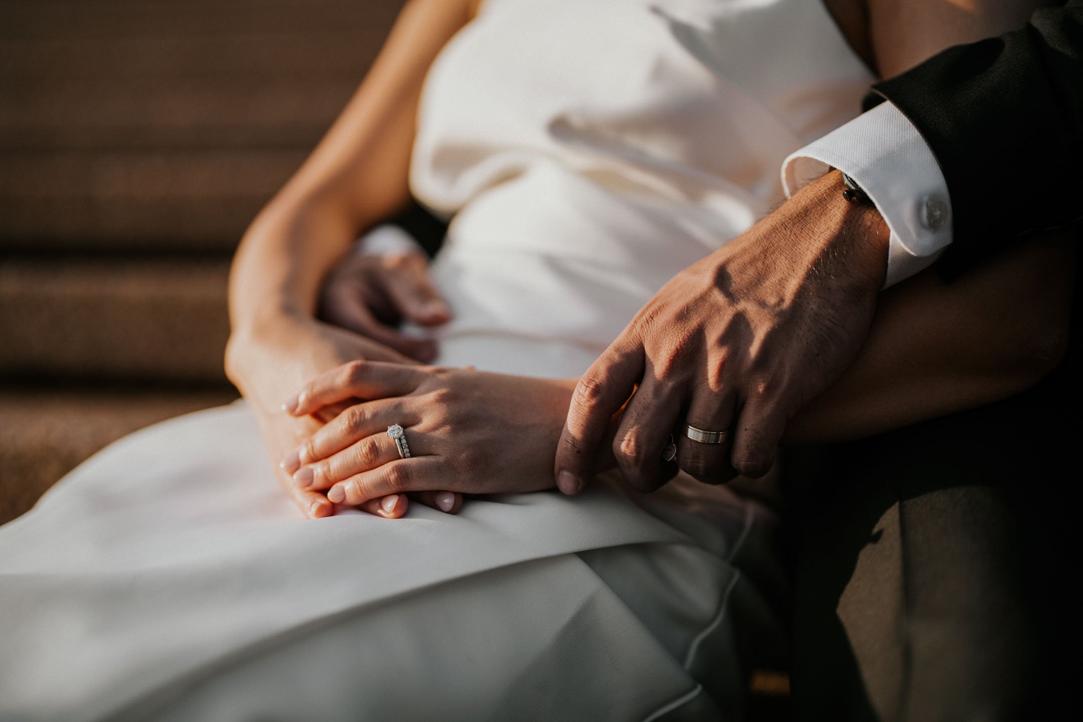 A couple holding hands during their wedding, showing the bride's engagement ring and the groom's wedding band.