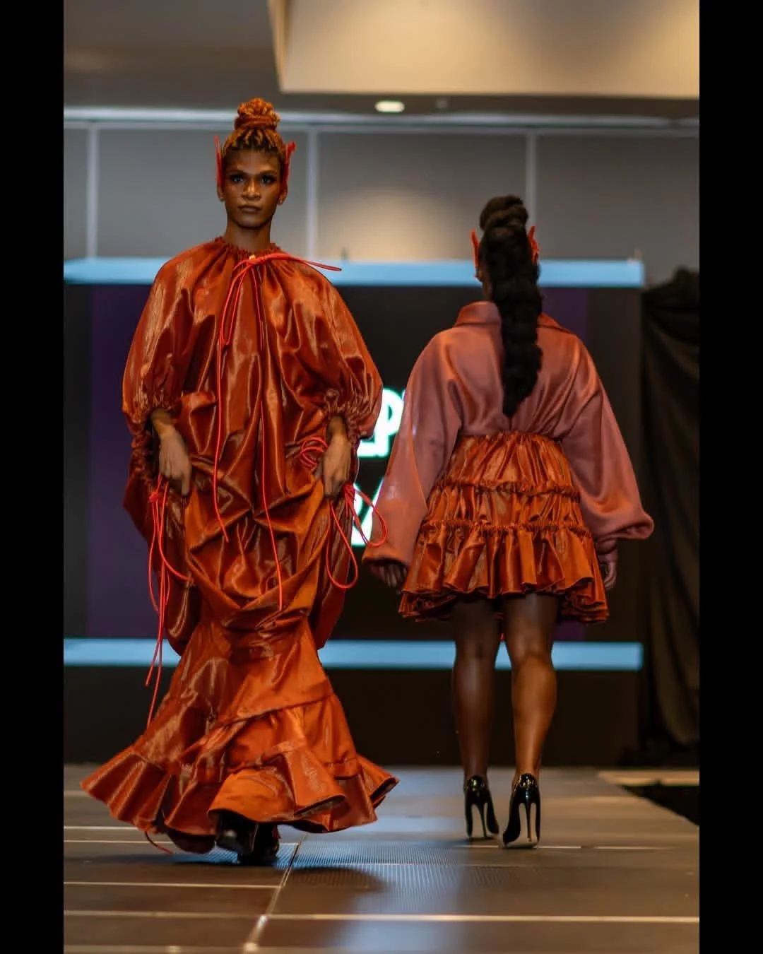 Two models in copper-toned designs crossing on a fashion runway