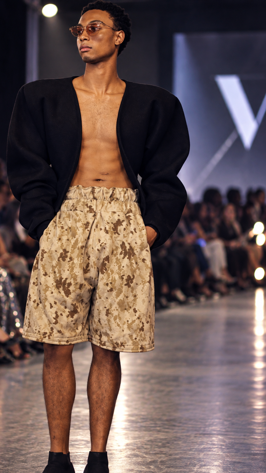 Runway model wearing an open black jacket, patterned trousers and sunglasses