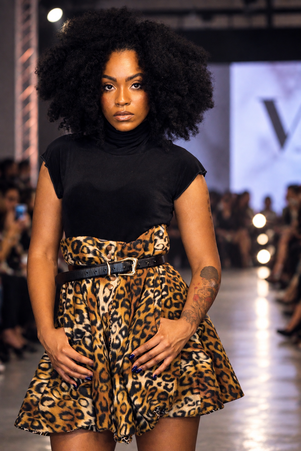 Runway model wearing a black top and belted leopard-print skirt