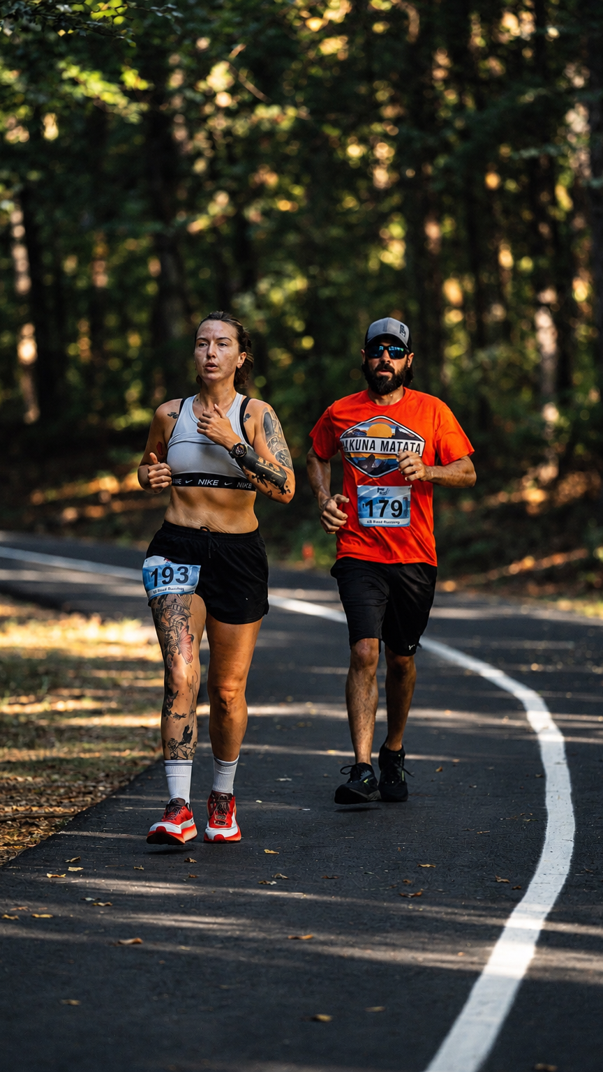 Two race participants running along a shaded paved trail