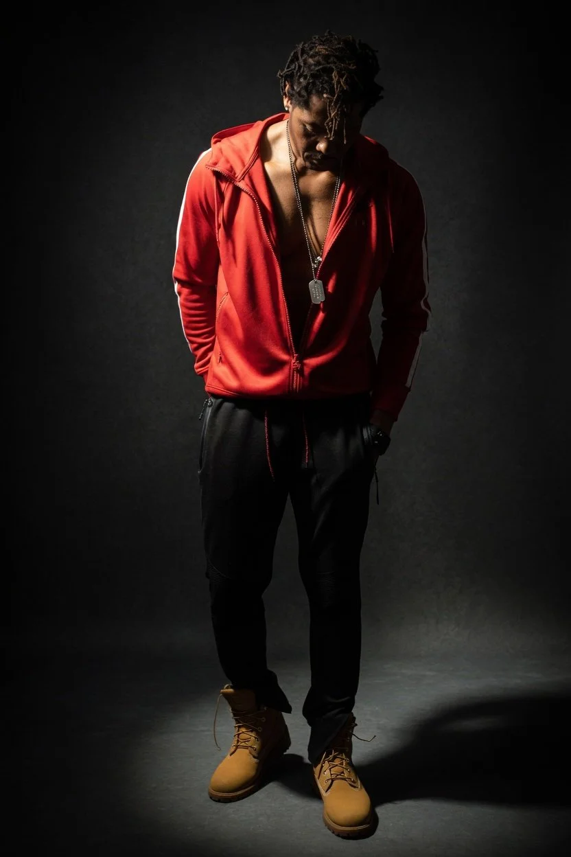 Dramatically lit studio portrait of a man wearing a red hoodie against a dark background