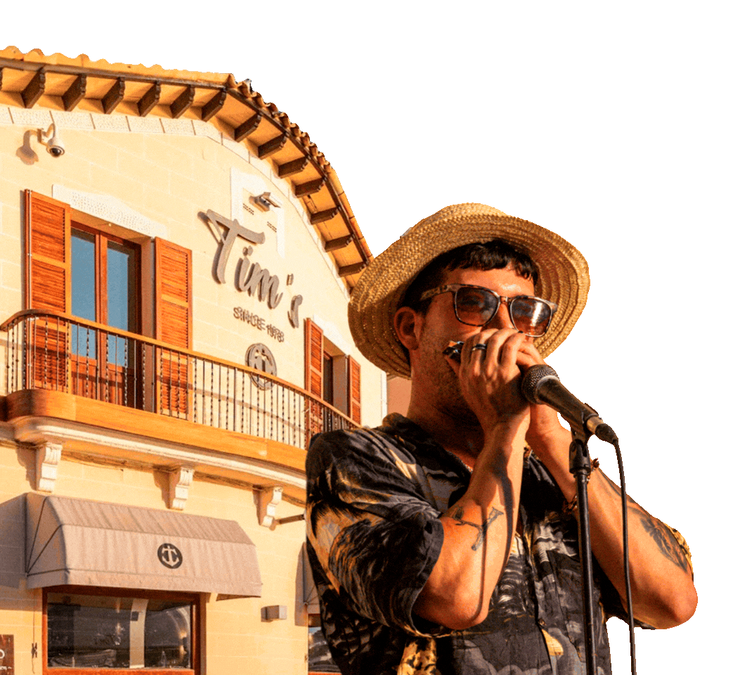 Hombre cantando con sombrero de paja en una terraza frente a un restaurante llamado "Tim's"