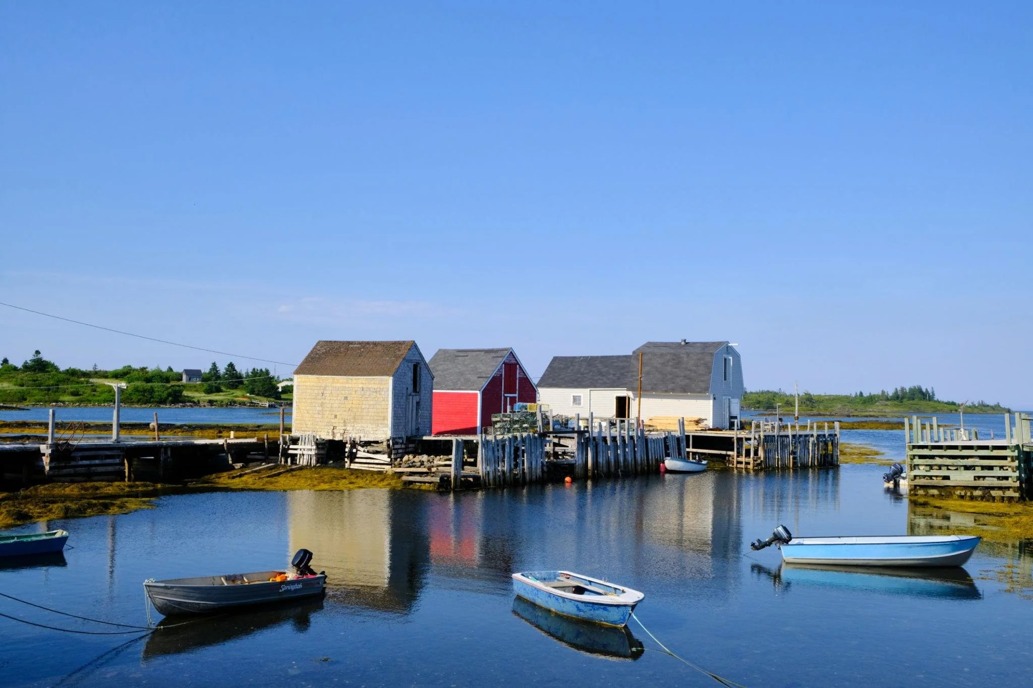 Small boats floating on calm water near wooden docks and colorful houses on an island with green trees in the background under a clear blue sky.