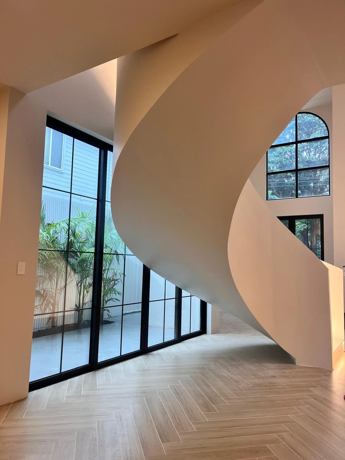 Modern interior with a curved white staircase, large floor-to-ceiling windows, and light wood flooring.