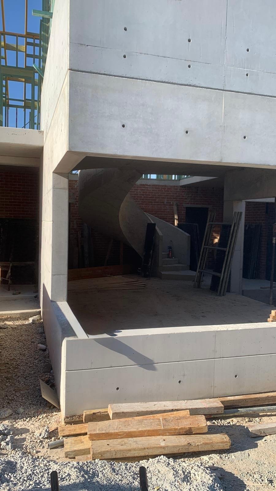 Construction site with a concrete staircase enclosed by concrete walls, with wood planks and construction materials on the ground.