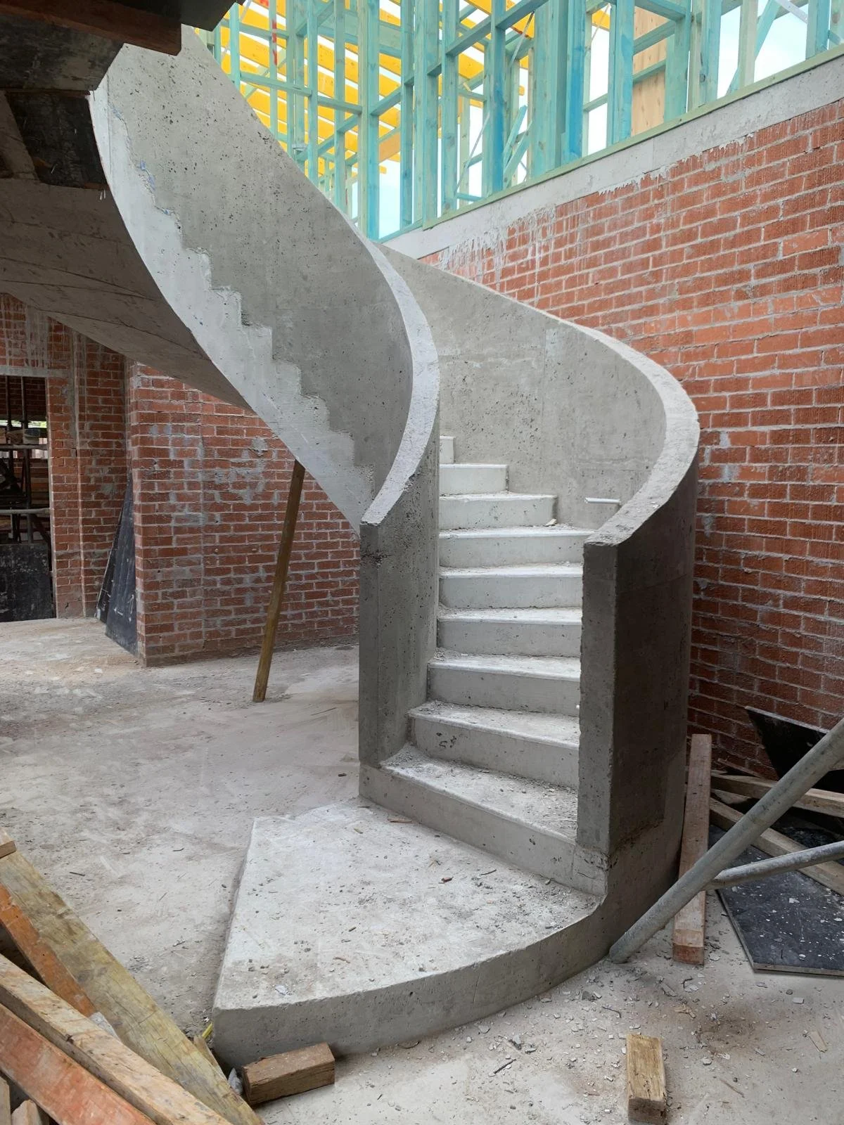 Concrete spiral staircase under construction inside a building with brick walls and exposed wooden framing.