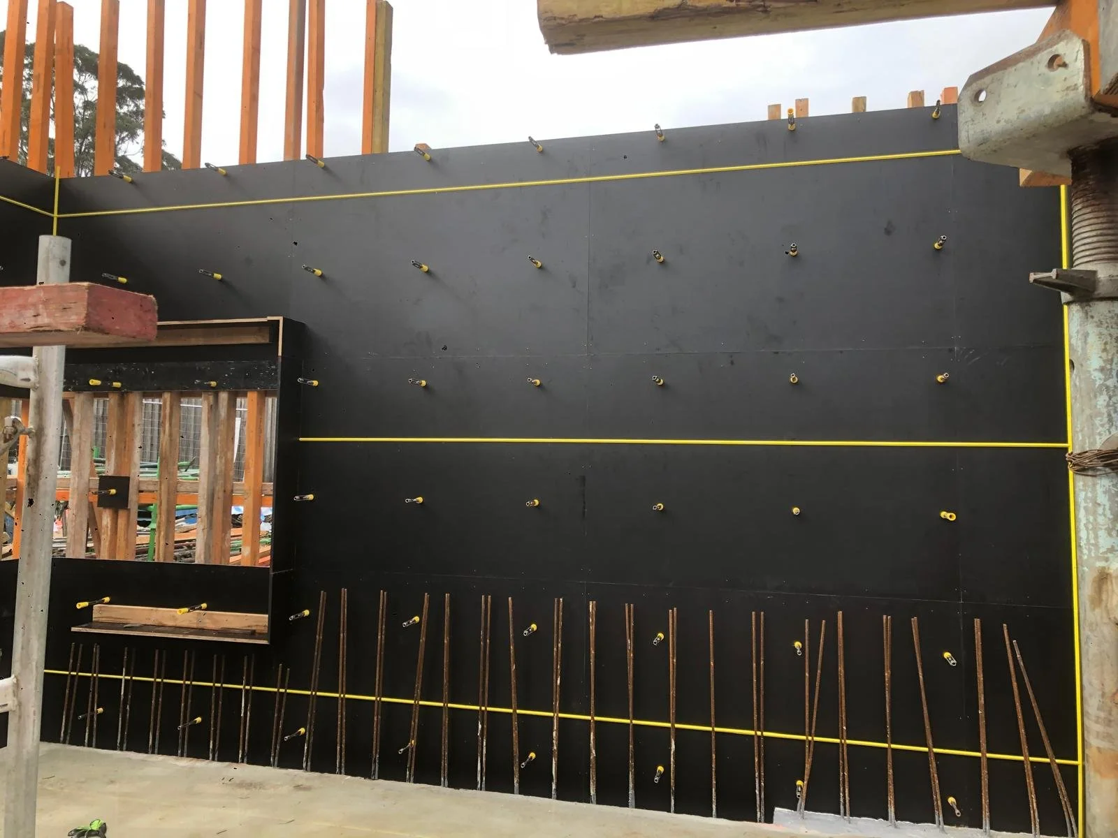 Construction site with black wall panels, yellow lines, metal rods, and wooden framing.