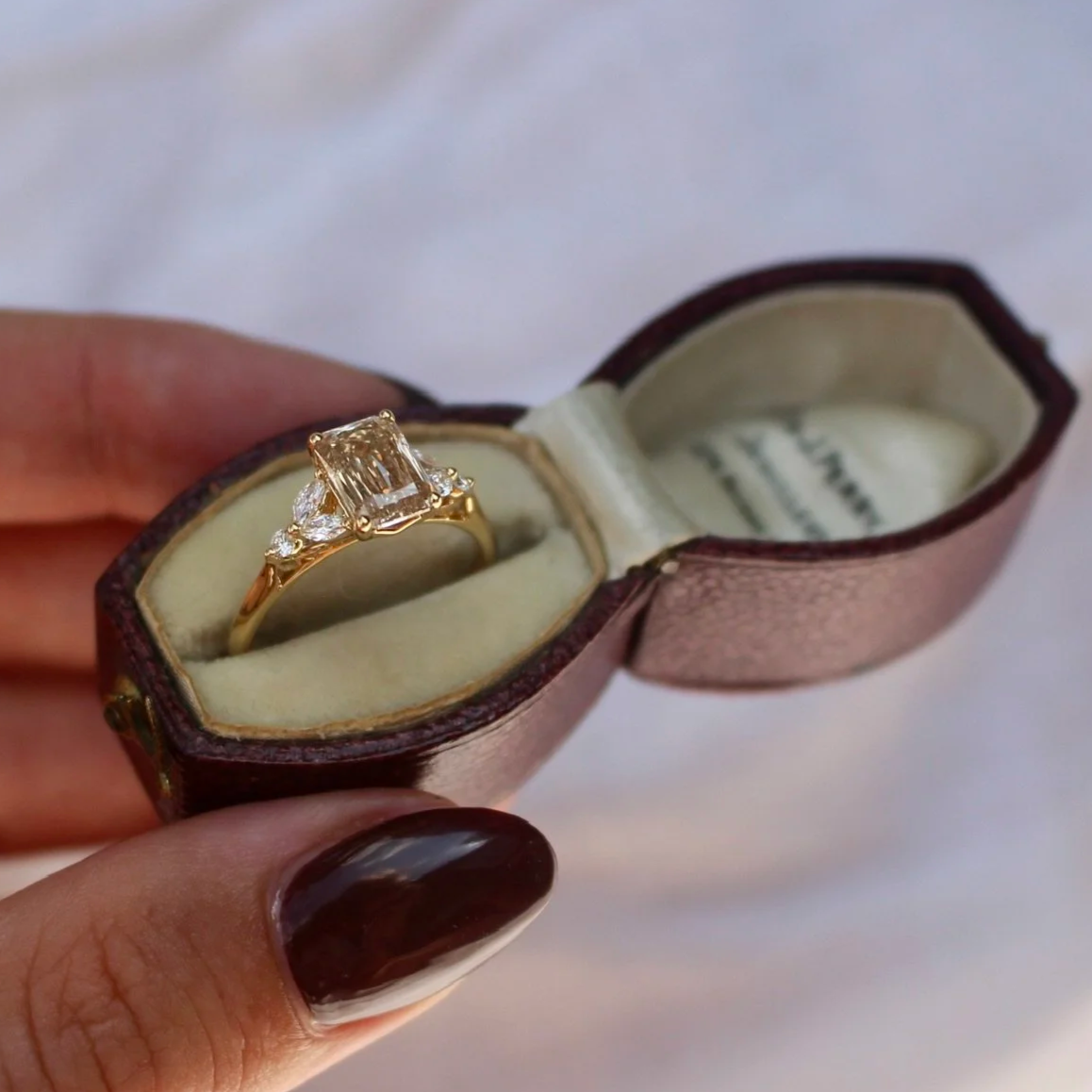 A gold ring with a rectangular diamonds is inside a vintage jewelry box.