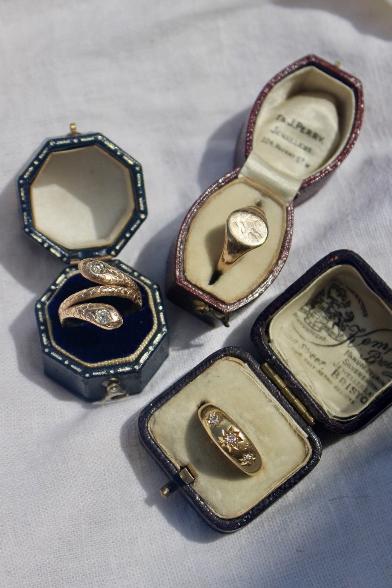 Vintage jewelry collection with rings and earrings in decorative boxes on a white fabric surface.