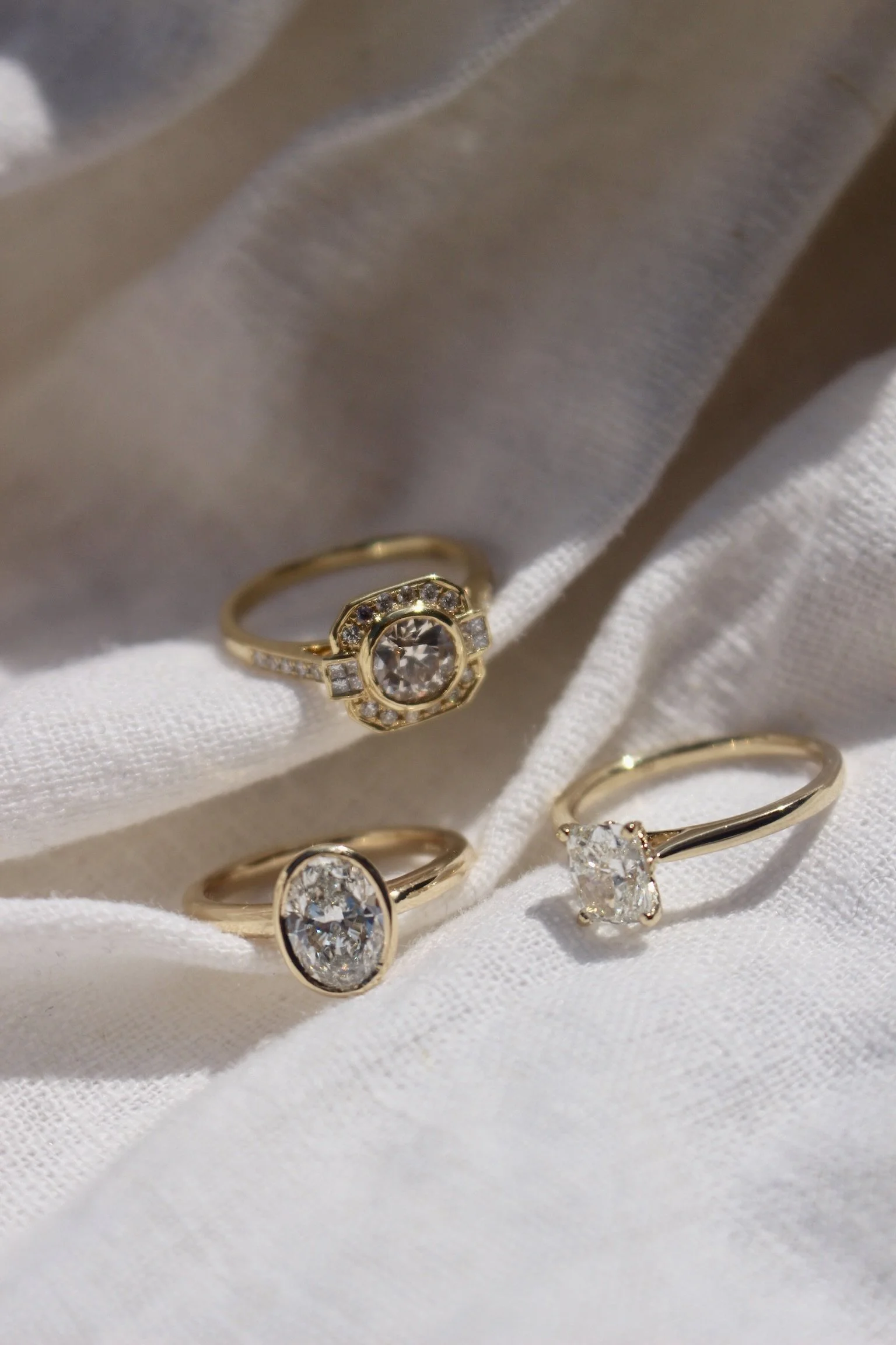 Close-up of multiple gold rings with large clear gemstones displayed on white fabric.