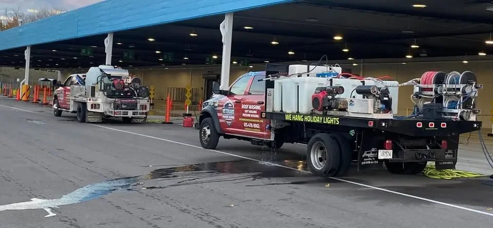 A row of fire trucks and service vehicles parked outside a building, with equipment on their flatbeds, including hoses and tools, and wet ground indicating recent water usage.