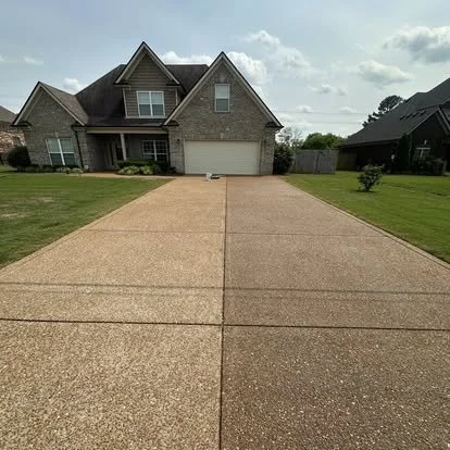 A suburban house with a paved driveway, green lawns, and partly cloudy sky.