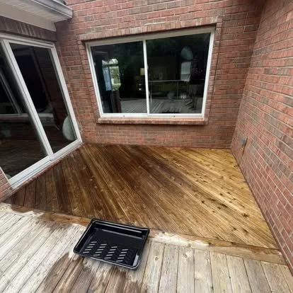 Partially renovated wooden deck with dark stained wood, brick wall, and a window.