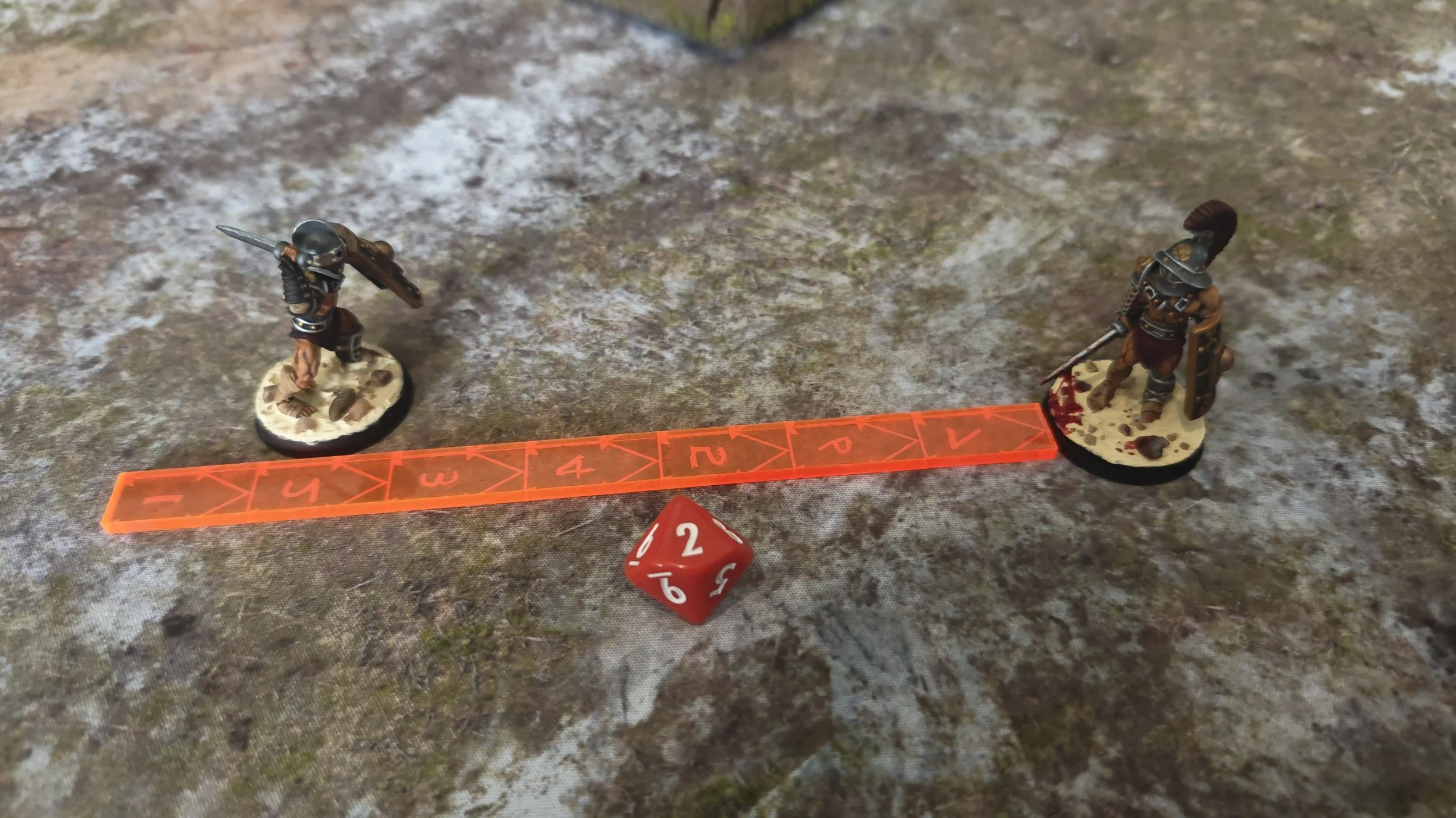 Two miniature warrior figurines on round bases, a measuring track, and a red die on a textured surface.